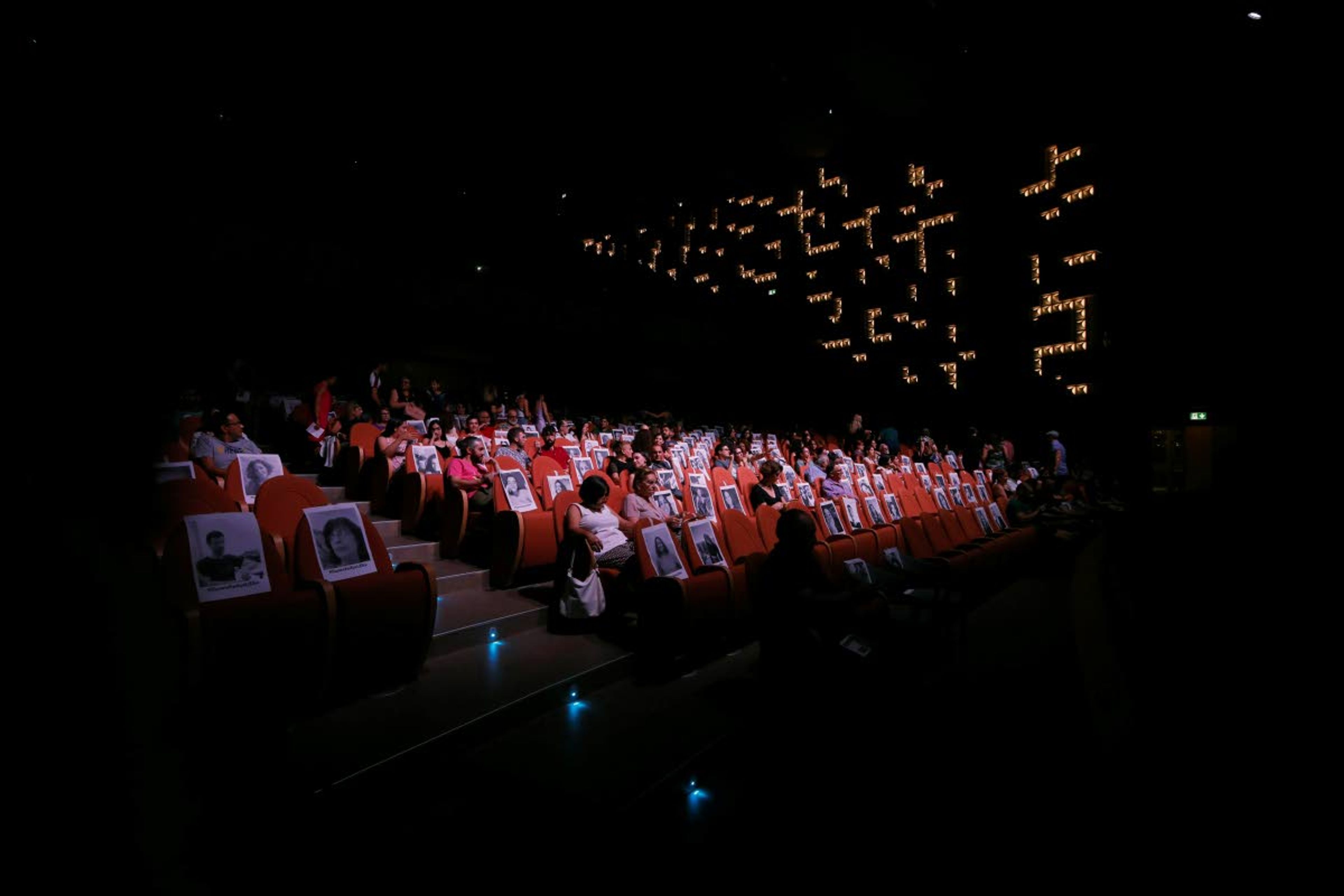 People sit among photographs of people printed on sheets of paper stuck on seats in order for the audience to social distance, at the Municipal Theater in capital Nicosia, Cyprus, Monday, July 27, 2020. A group of actors are performing a number of short plays dealing with the goings-on during coronavirus lockdown conditions that Cyprus imposed between March and May of this year. (AP Photo/Petros Karadjias)