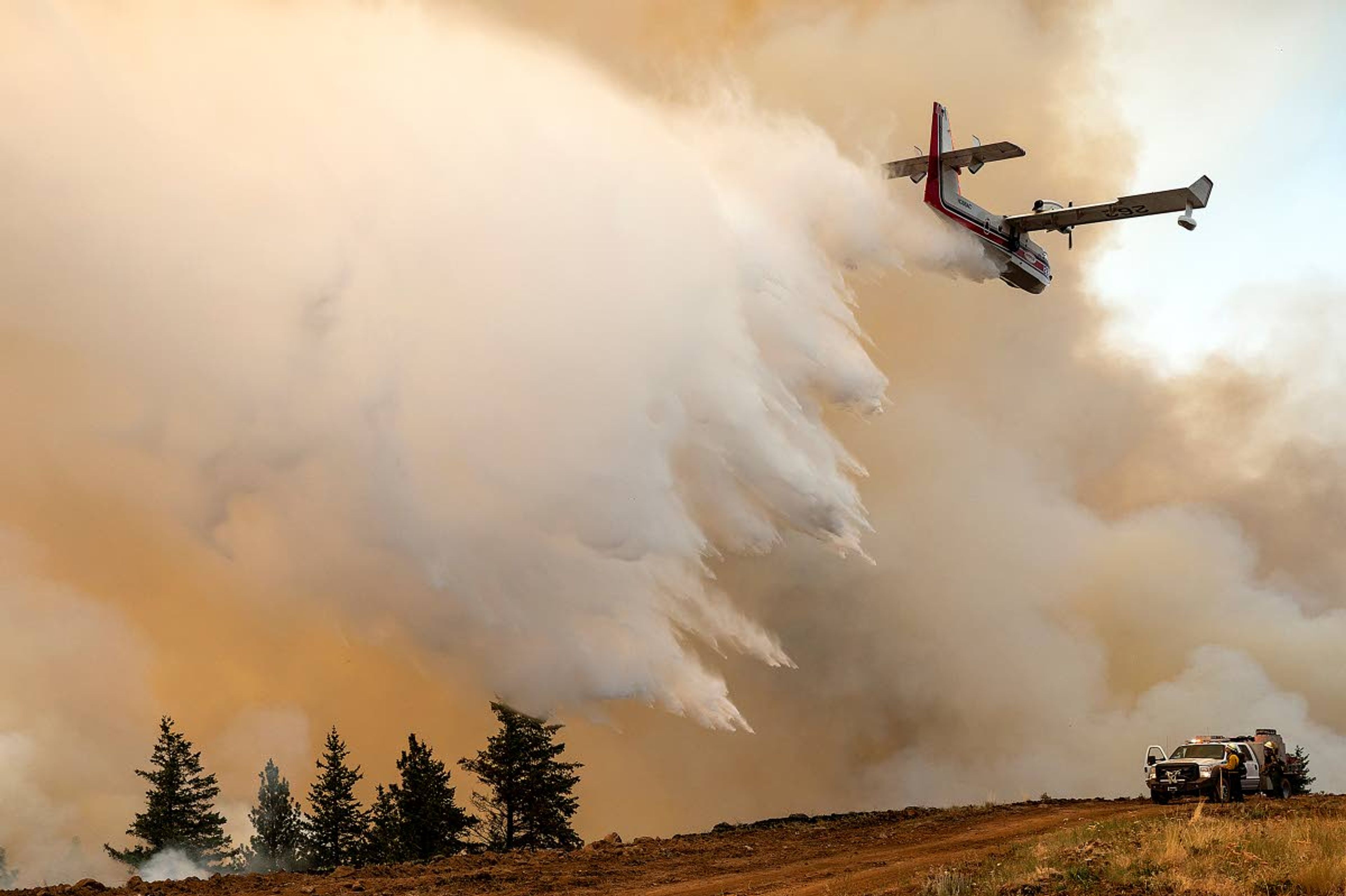 A scoop plane drops water onto burning ridge where a fire line had been created by crews of wildland firefighters on Monday afternoon at the Lick Creek Fire southwest of Asotin.