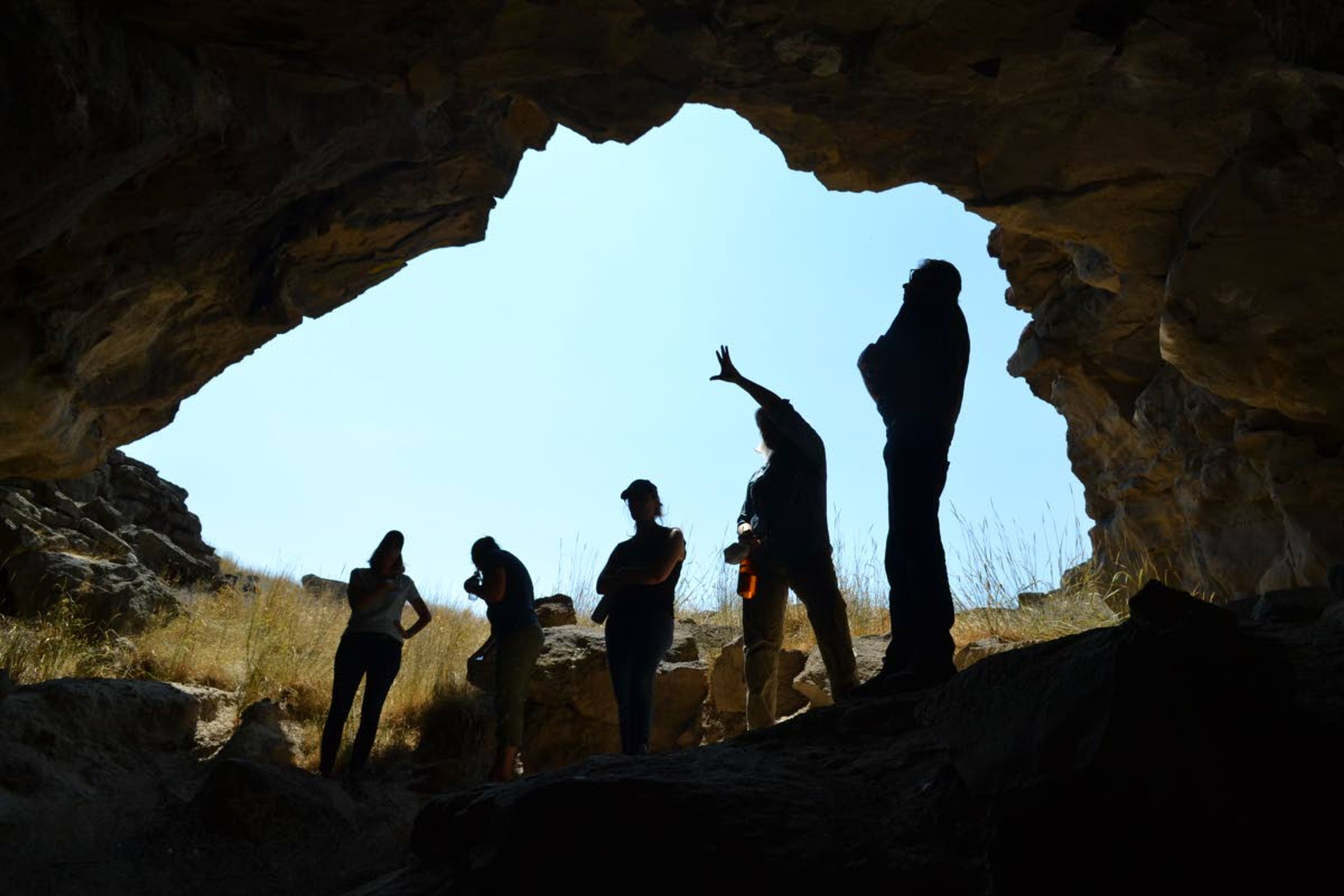 A view from inside Owl Cave looking out shows Idaho National Laboratory archaeologist Suzann Henrikson pointing out things to Museum of Idaho staff members.