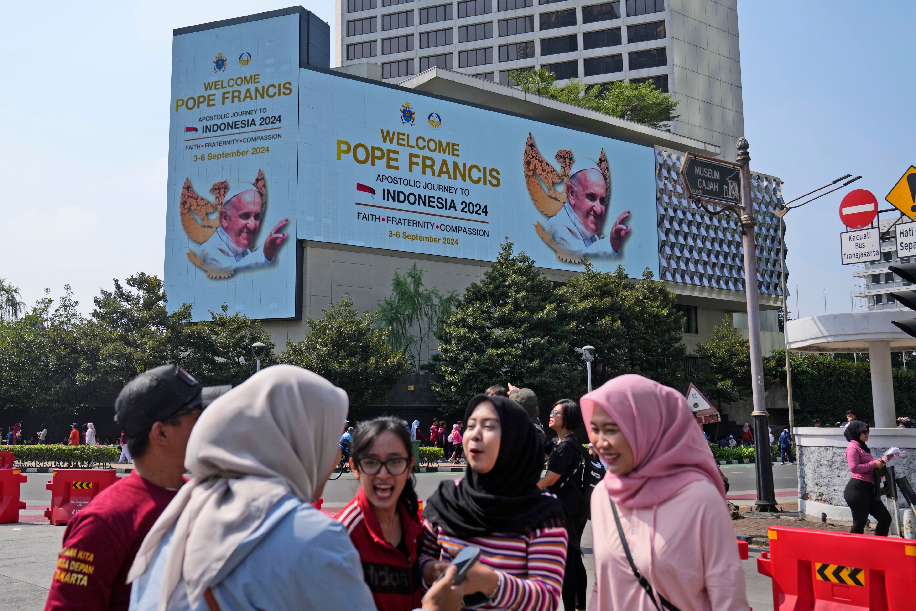 Muslim women chat as a large digital advertisement board with a welcoming message for Pope Francis is displayed on the facade of a building nearby in Jakarta, Sunday, Sept. 1, 2024, ahead of his visit to Indonesia from Sept. 3-6.