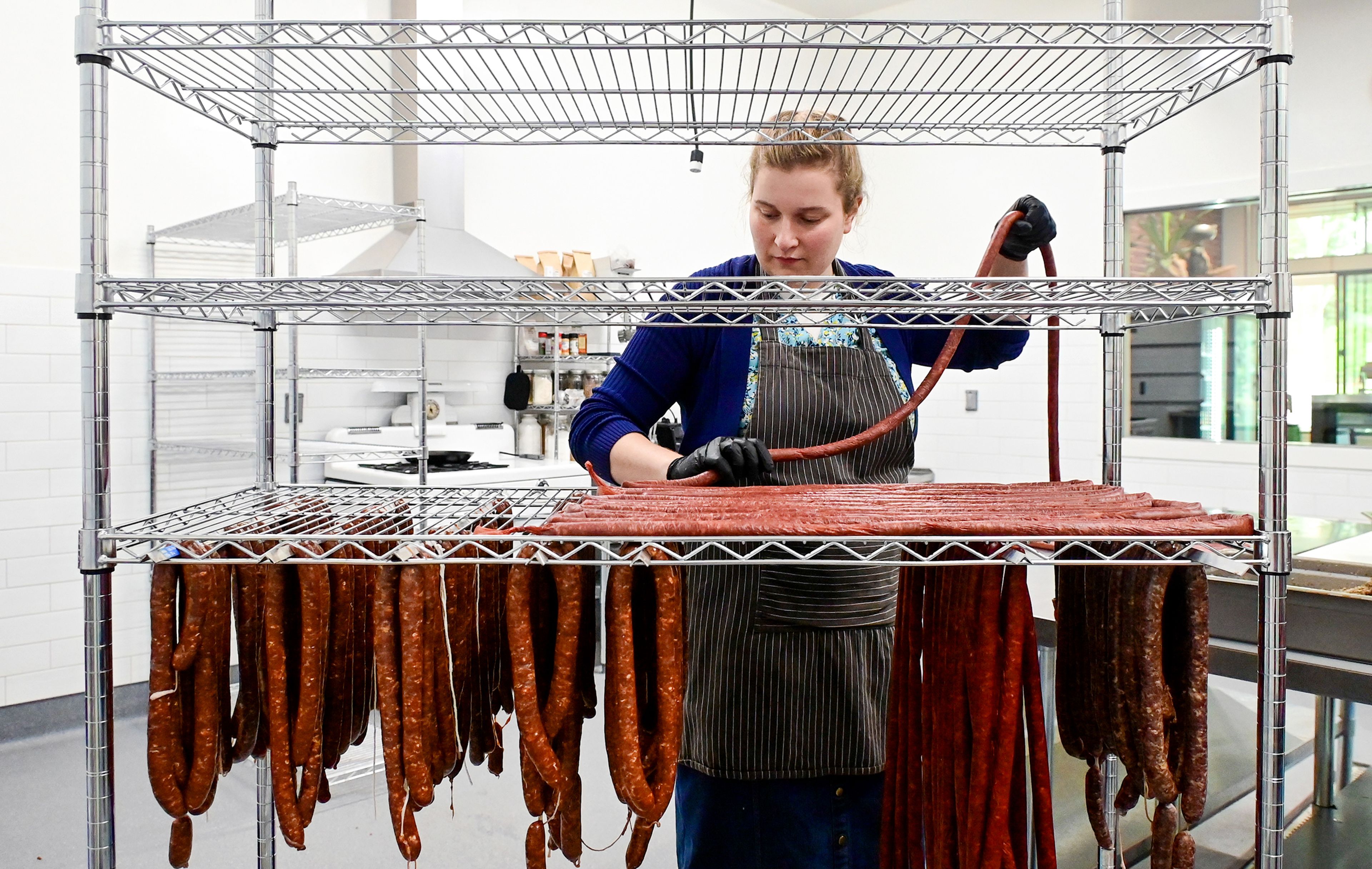 Hanna Moore lays out freshly stuffed meat sticks to prepare them for hanging for 24 hours, and then smoking for another six hours, at The Butcher Shop on Friday in Deary.