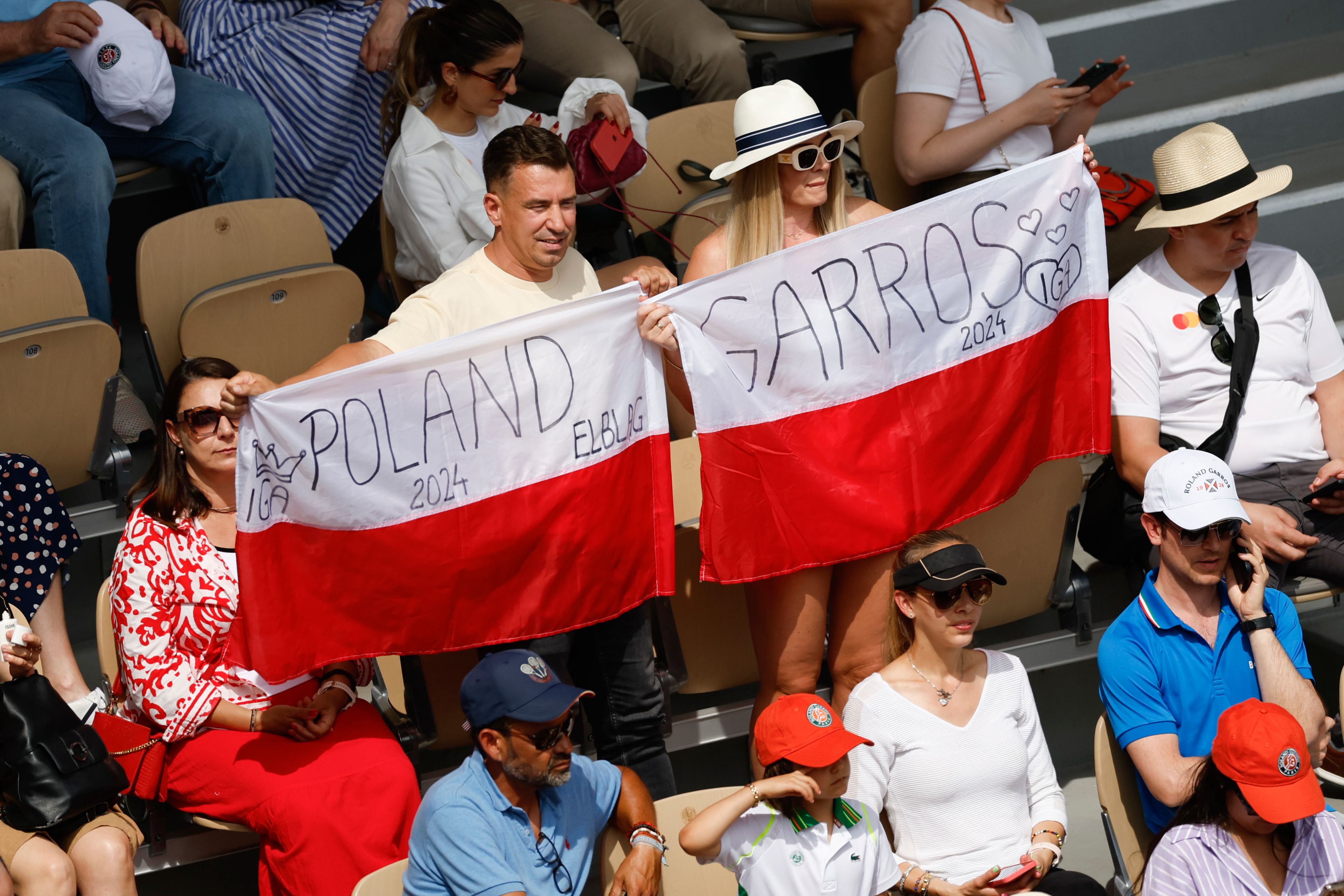 Fans of Poland's Iga Swiatek hold the national flag as she against Italy's Jasmine Paolini during the women's final of the French Open tennis tournament at the Roland Garros stadium in Paris, France, Saturday, June 8, 2024.