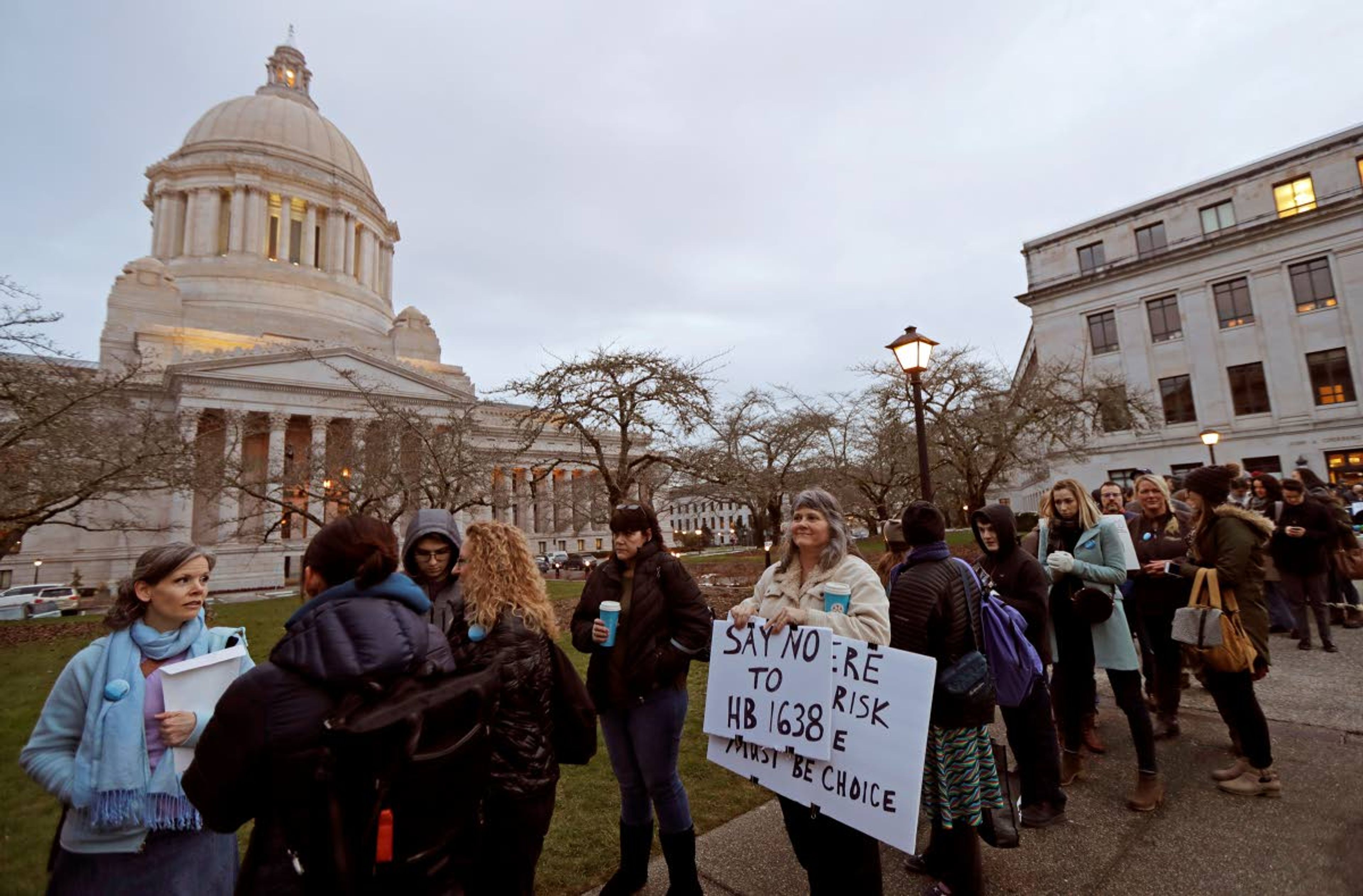 Kebby Johnson (center) of Spokane holds a sign that reads “Say No to HB 1638,” as she waits in line Friday to attend a public hearing in Olympia.