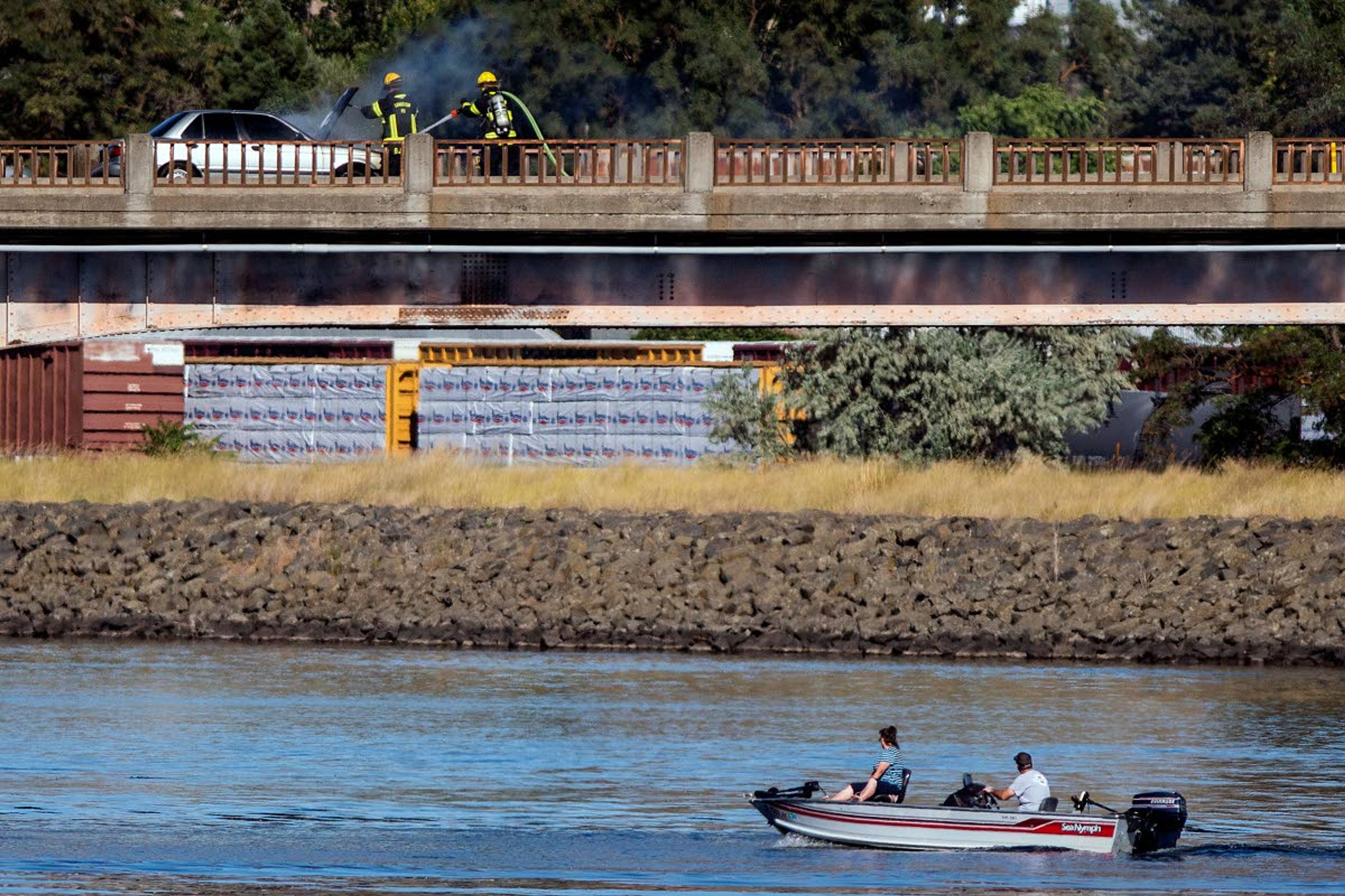 Boaters look on as a pair of firefighters from the Lewiston Fire Department spray water onto a sedan that caught fire Saturday afternoon on the Memorial Bridge. The fire stopped traffic in both directions for about 20 minutes.