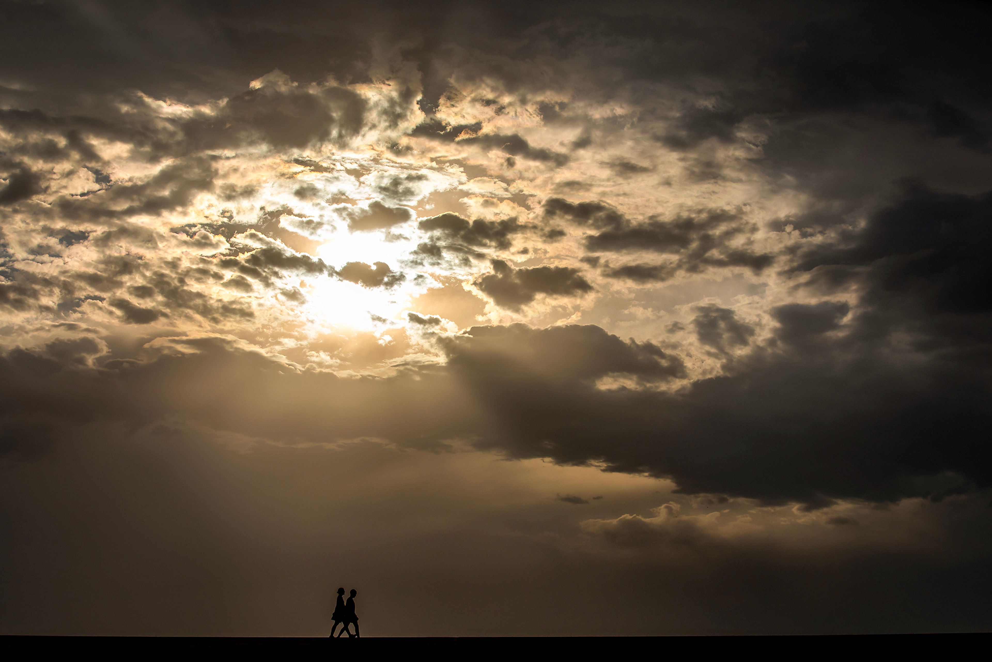 People walk down the Lewiston Levee Parkway Trail as the sun shines from between the clouds in the aftermath of a storm that blew across the region Wednesday in Lewiston. The storm featured wind gusts up to 40 mph that blew massive dust clouds through the region. Tree branches were blown down and several minor power outages were reported.