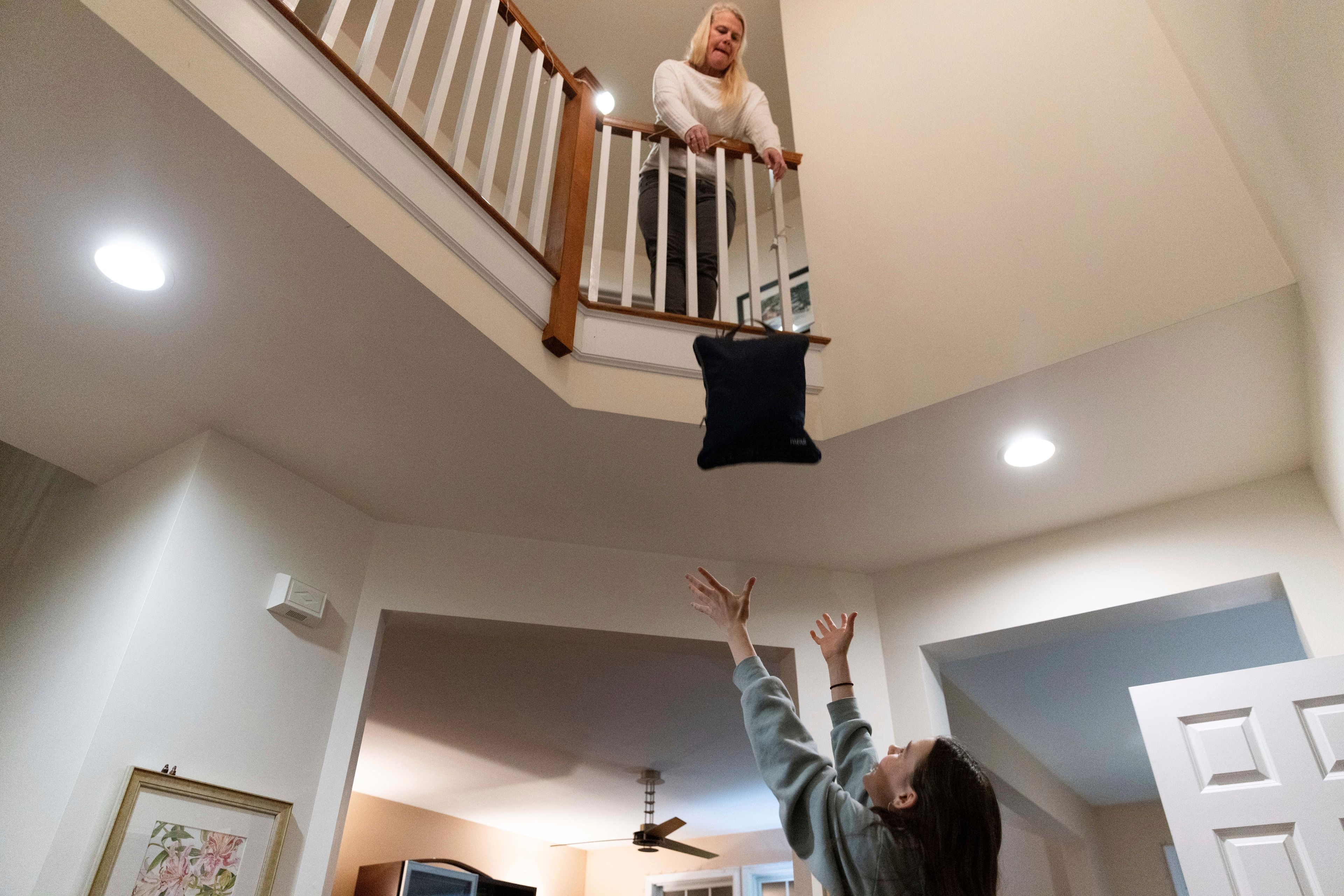 Steph Bulkeley throws her daughter, Sutton, a bag of clothes while packing for a ski vacation, Friday, Feb. 16, 2024, in Westport, Conn. It is hard to be a teenager today without social media. For those trying to stay off social platforms at a time when most of their peers are immersed, the path can be challenging, isolating and at times liberating. It can also be life-changing.