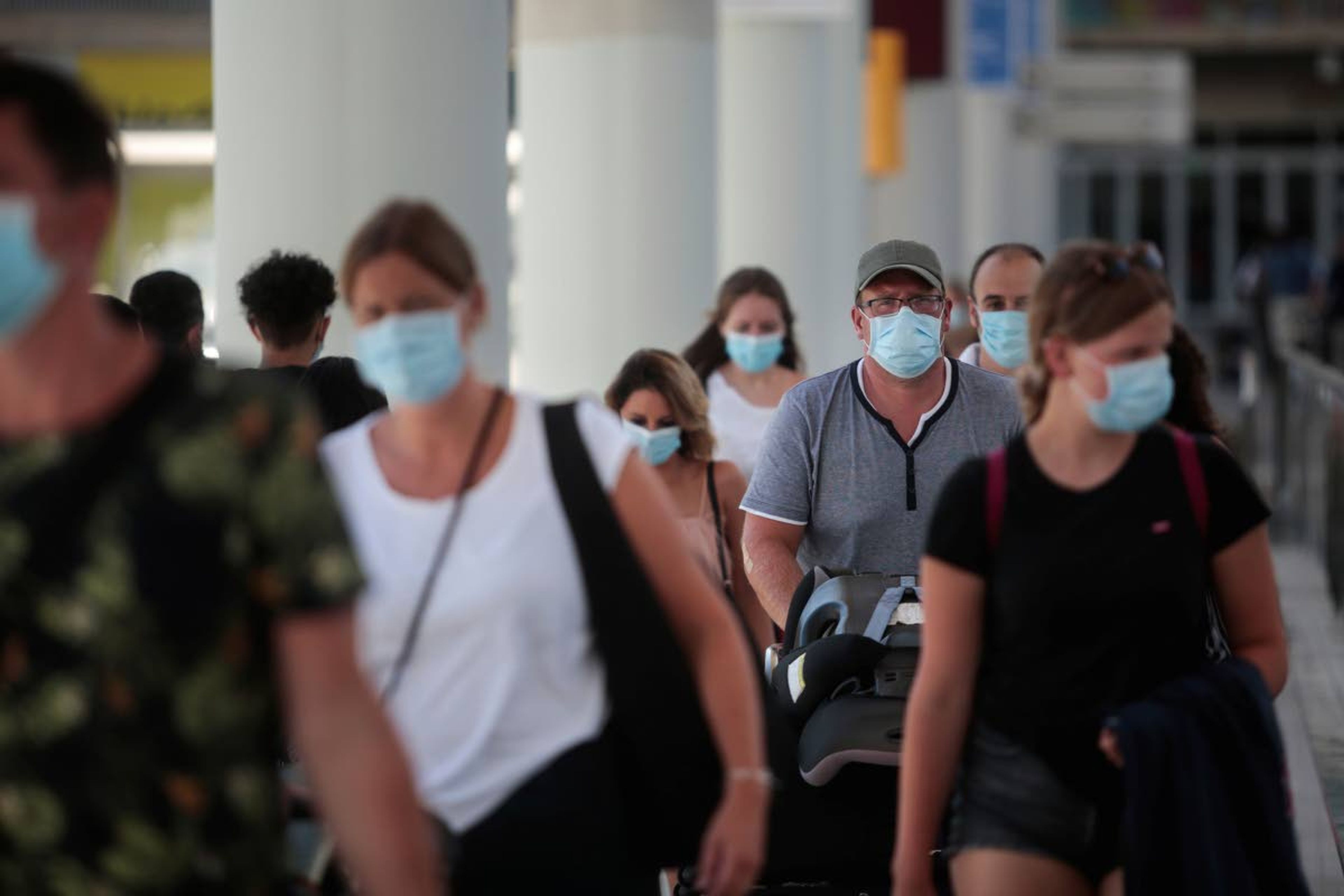 Passengers wearing face masks arrive at Son Sant Joan airport on the Spanish Balearic Island of Mallorca, Spain, Monday, July 27, 2020. Britain has put Spain back on its unsafe list and announced Saturday that travelers arriving in the U.K. from Spain must now quarantine for 14 days. (AP Photo/Joan Mateu)