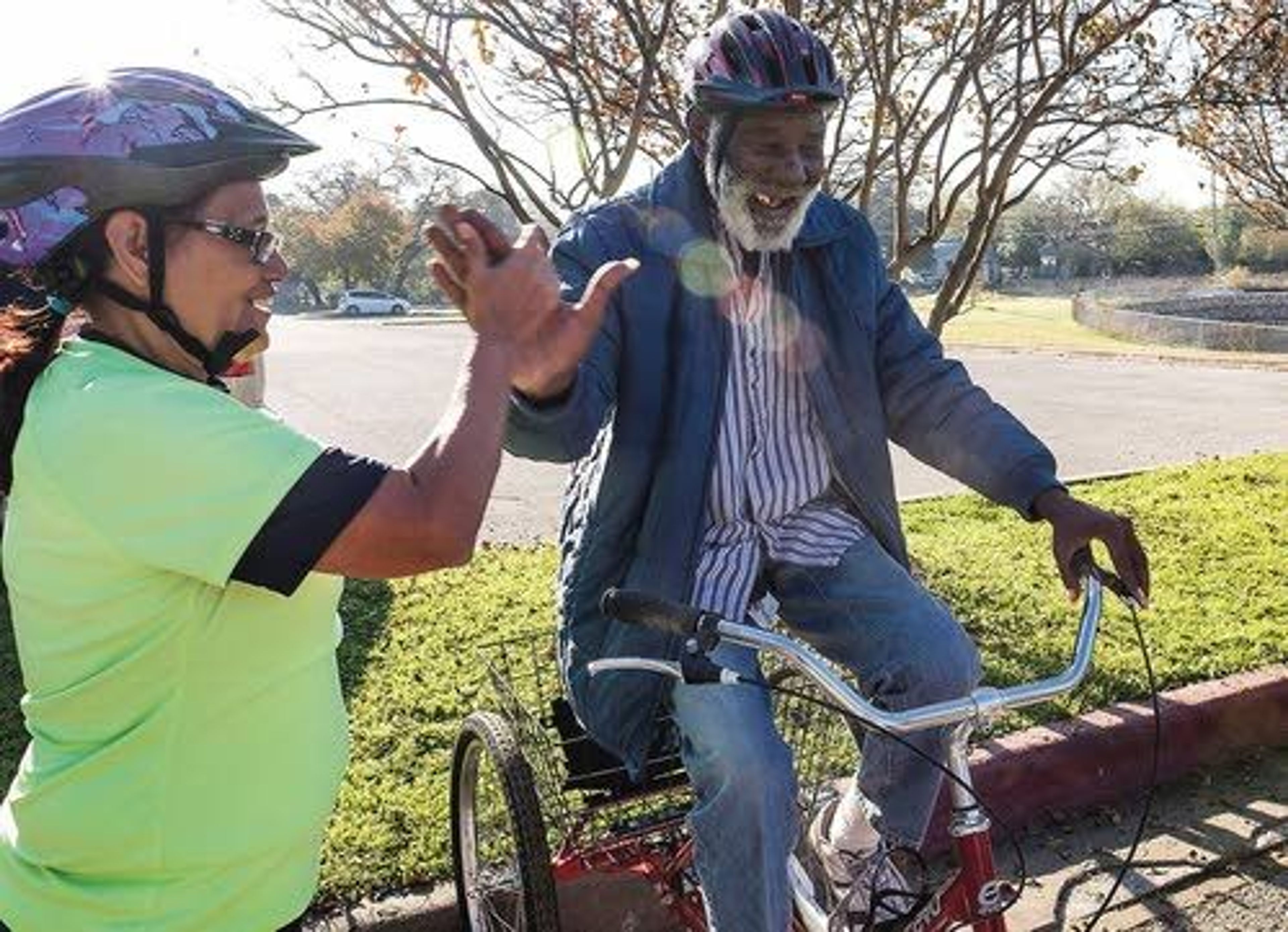 ABOVE: Bike Austin instructor Preston Tyree (right) helps push and offers instructions to Bertha Sellers, 75, as she pedals her trike bike on a ride with the Ghisallo Cycling Initiative. LEFT: Maria G. Pena, 63, (left) high fives James Maxwell, 68, (right) after the two finished a ride with the trike program.