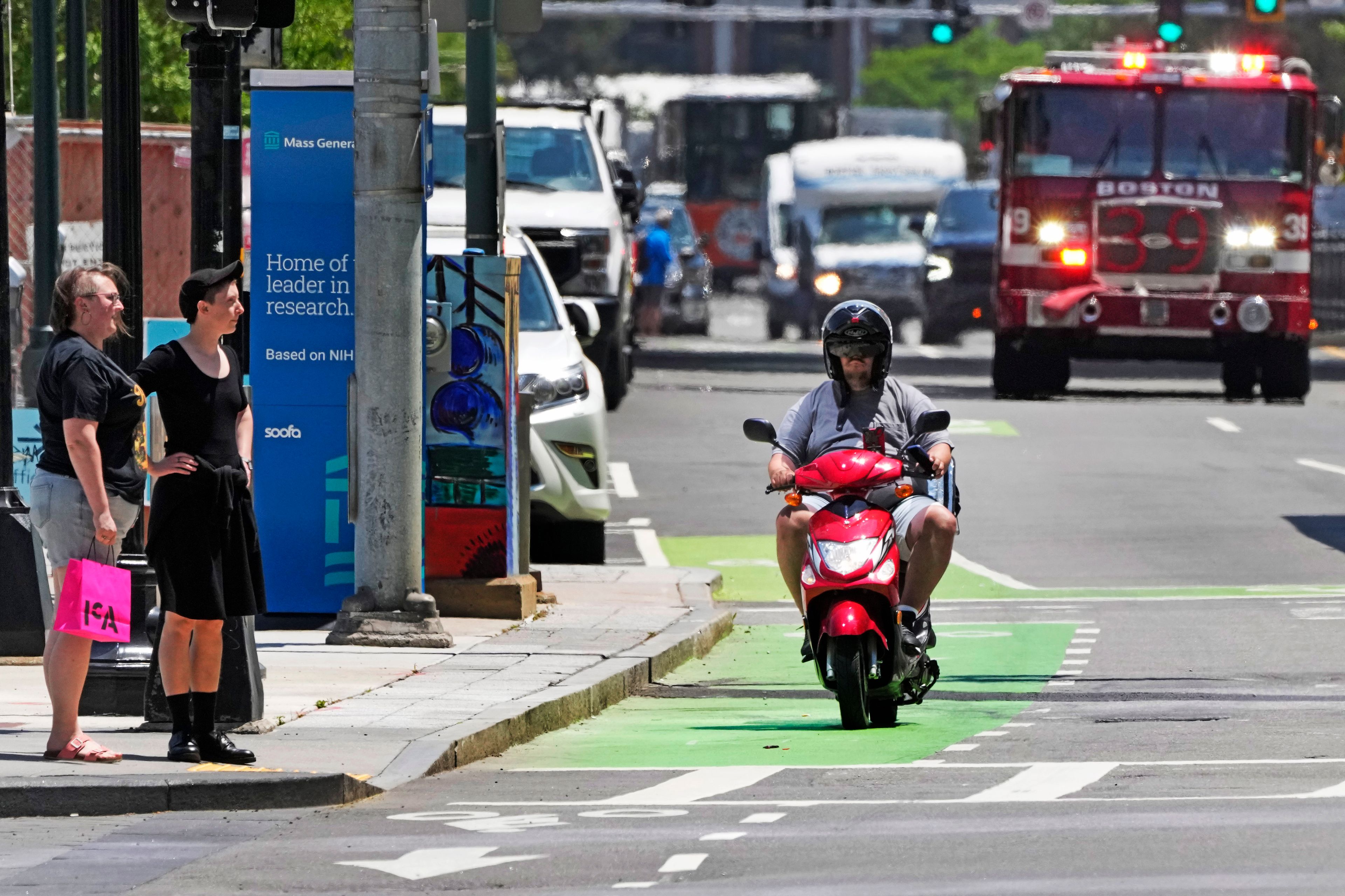 A delivery driver on a scooter keeps pace with a fire engine on a call in the Seaport District, Friday, June 7, 2024, in Boston. A soaring demand for food delivered fast has spawned small armies of couriers in a growing number of cities where delivery scooters, motorcycles and mopeds zip in and out of traffic and hop onto sidewalks alongside startled pedestrians racing to drop off salads and sandwiches.