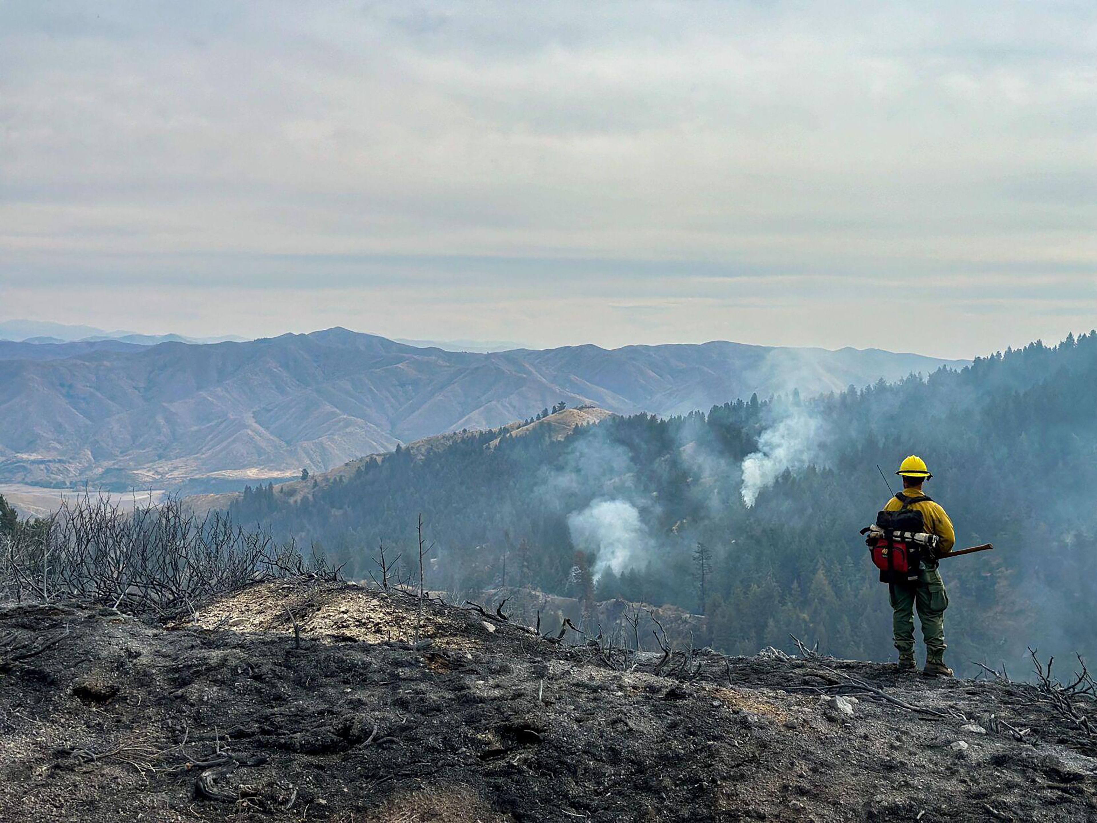 A firefighter on a ridge looks down at smoke in timber from the Valley Fire.