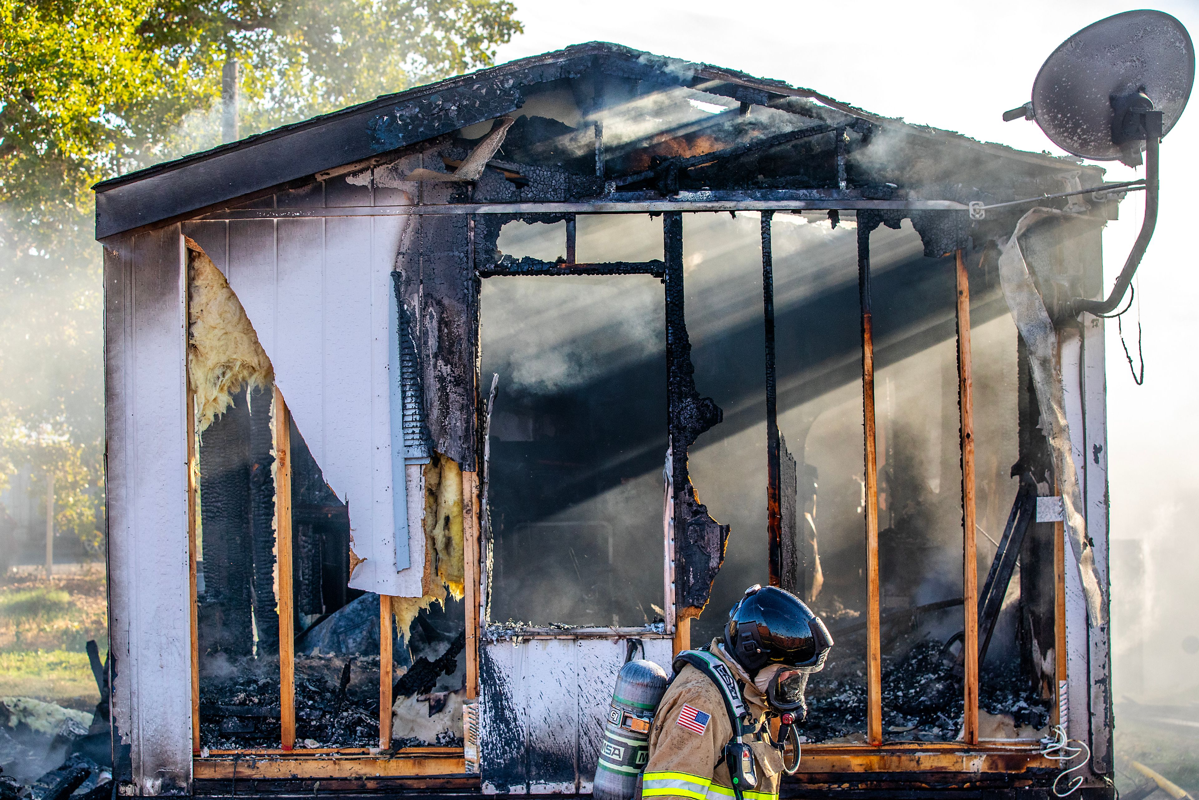 A firefighter walks past the smoking remains of a mobile home Thursday off 13th Street in Clarkston. Firefighters responded to the fully engulfed mobile home at 2:40 p.m. Thursday. The fire leaped and also destroyed a small pickup truck and a neighboring trailer, all of which appeared to be a total loss.