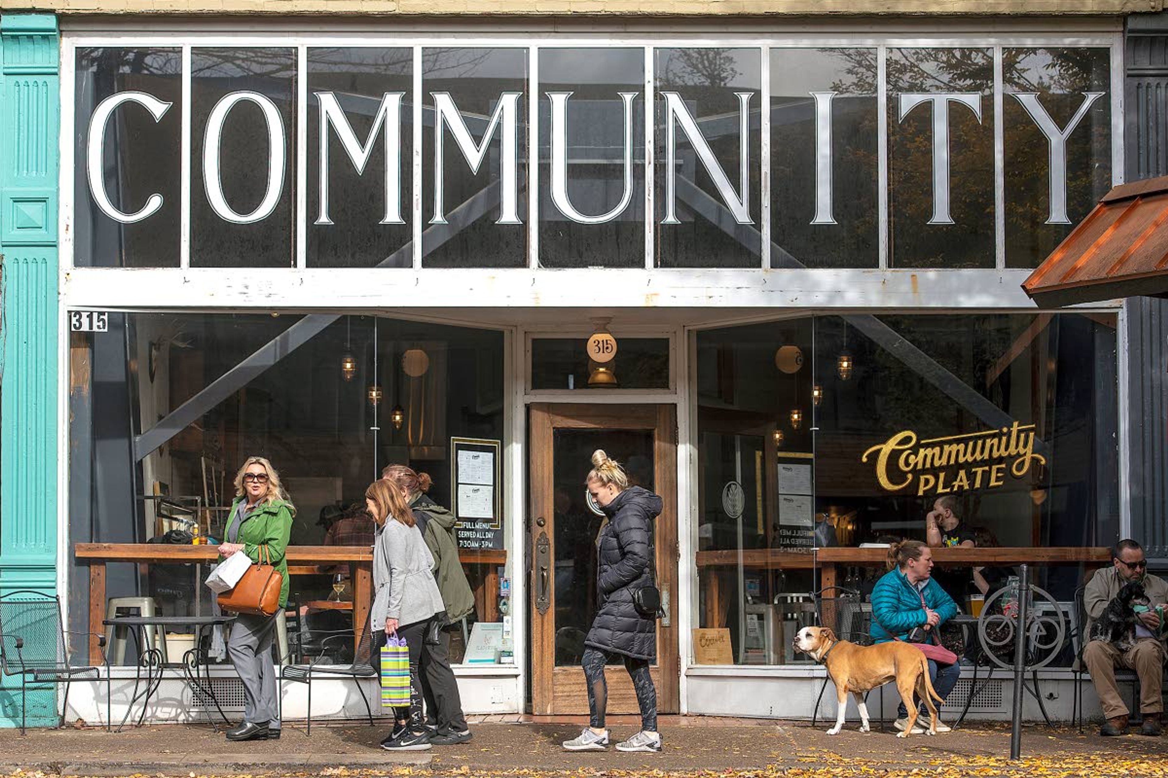 People (and dogs) walk, sit and stand outside Community Plate in downtown McMinnville. Because of its reasonable prices and selection of fresh locally sourced foods, the breakfast and lunch restaurant is popular with locals.