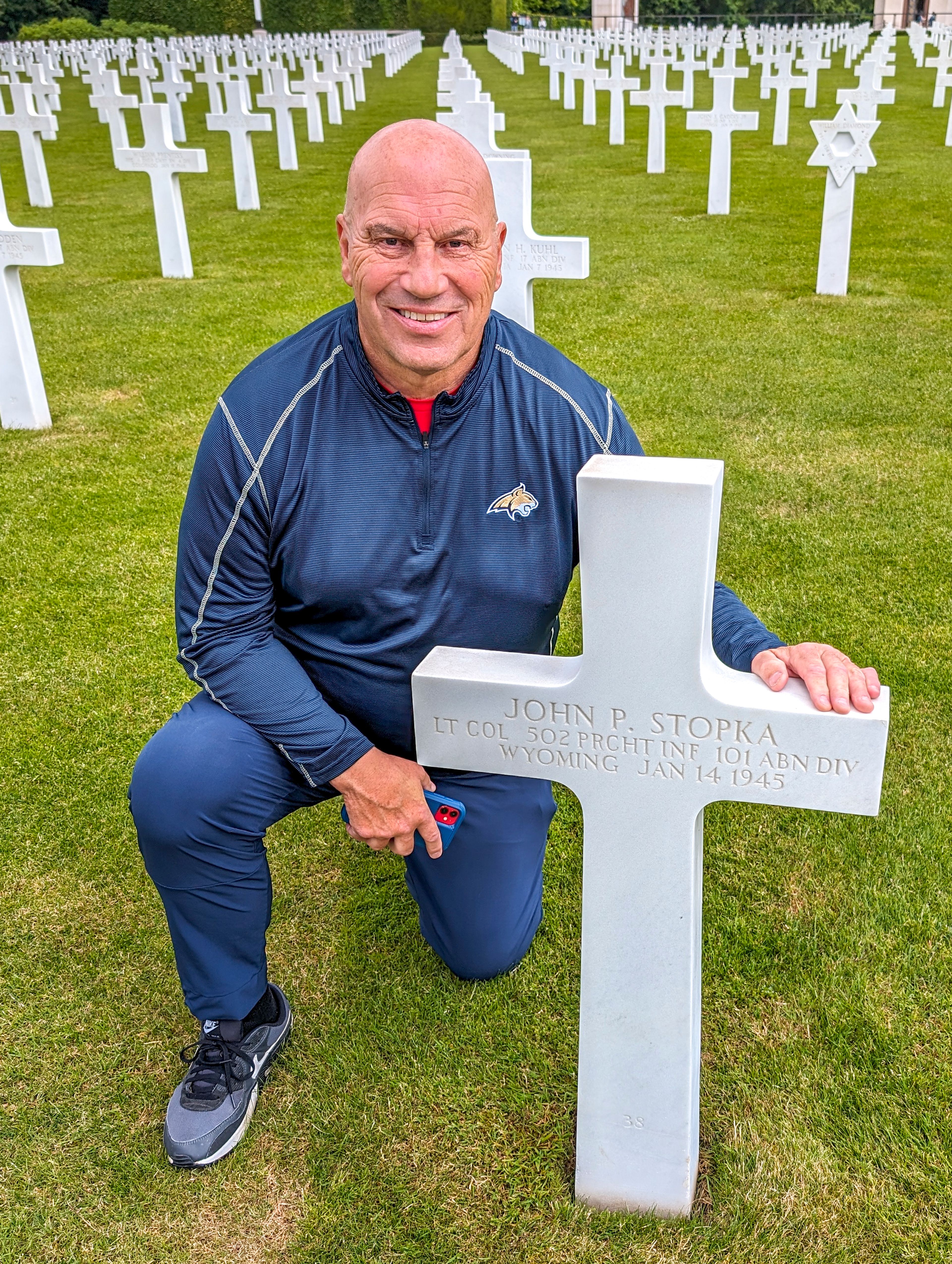 Mike Kramer kneels beside the grave of John Stopka in the Luxembourg American Cemetery.