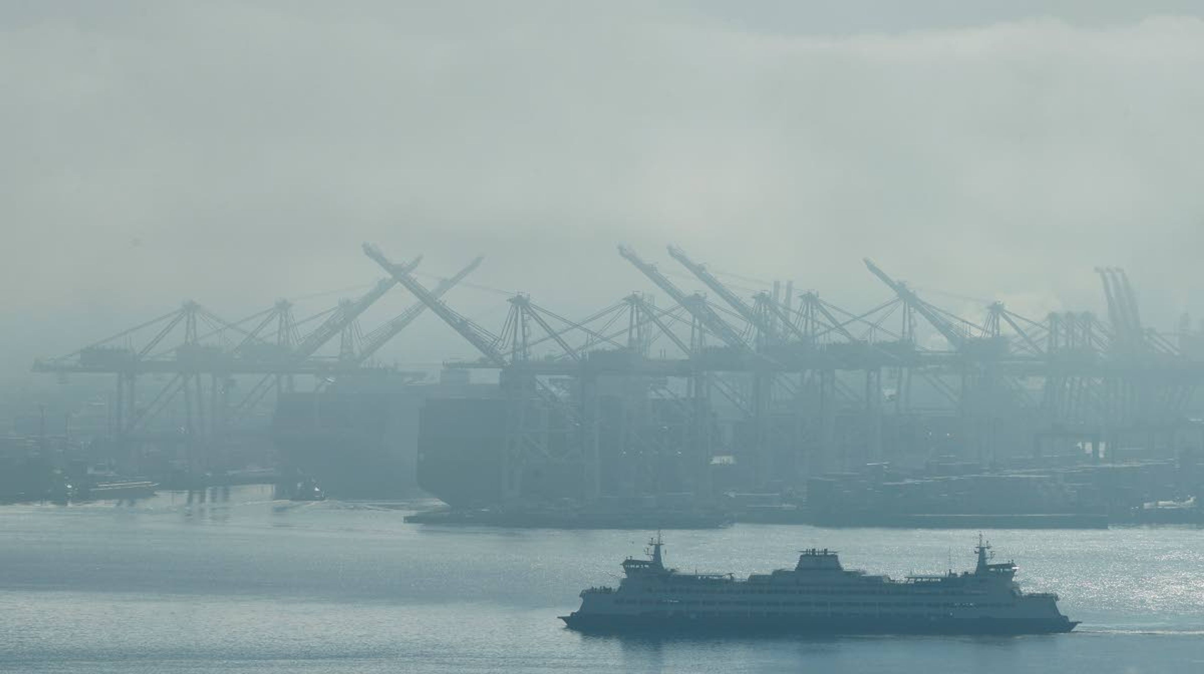 In this photo taken Dec. 31, 2018, a Washington state ferry sails on a foggy day near cranes at the Port of Seattle. Democrats in the Washington House released their two-year transportation budget proposal Monday, March 25, 2019, which included spending for projects such as a new hybrid-electric ferry and the conversion of two others. (AP Photo/Ted S. Warren)