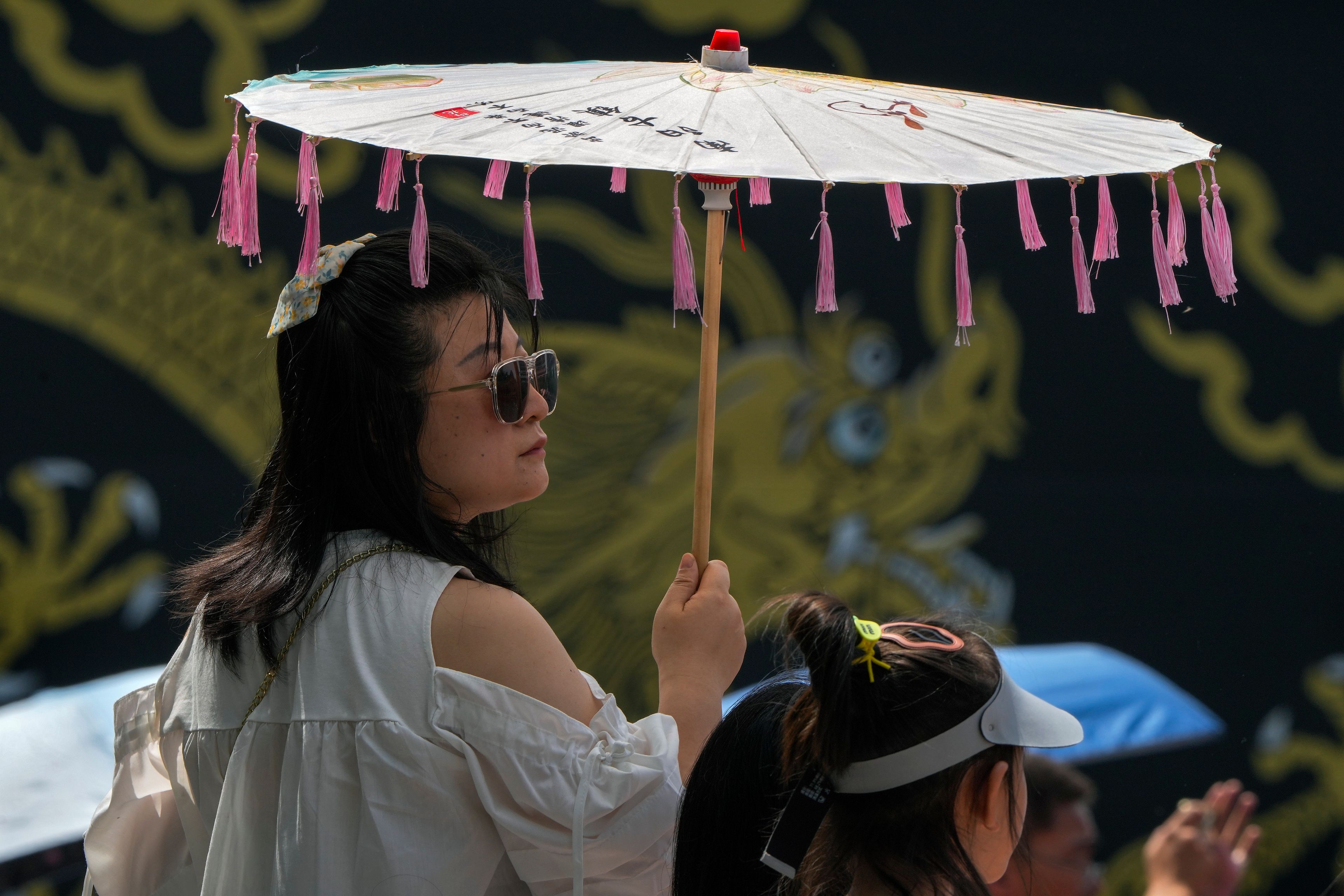 A woman carries an umbrella to shield from the sun as residents watch the Dragon Boat race during the Dragon Boat festival at a canal in Tongzhou, on the outskirts of Beijing, Monday, June 10, 2024. The Duanwu festival, also known as the Dragon Boat festival, falls on the fifth day of the fifth month of the Chinese lunar calendar and is marked by celebrations like eating rice dumplings and racing dragon boats.