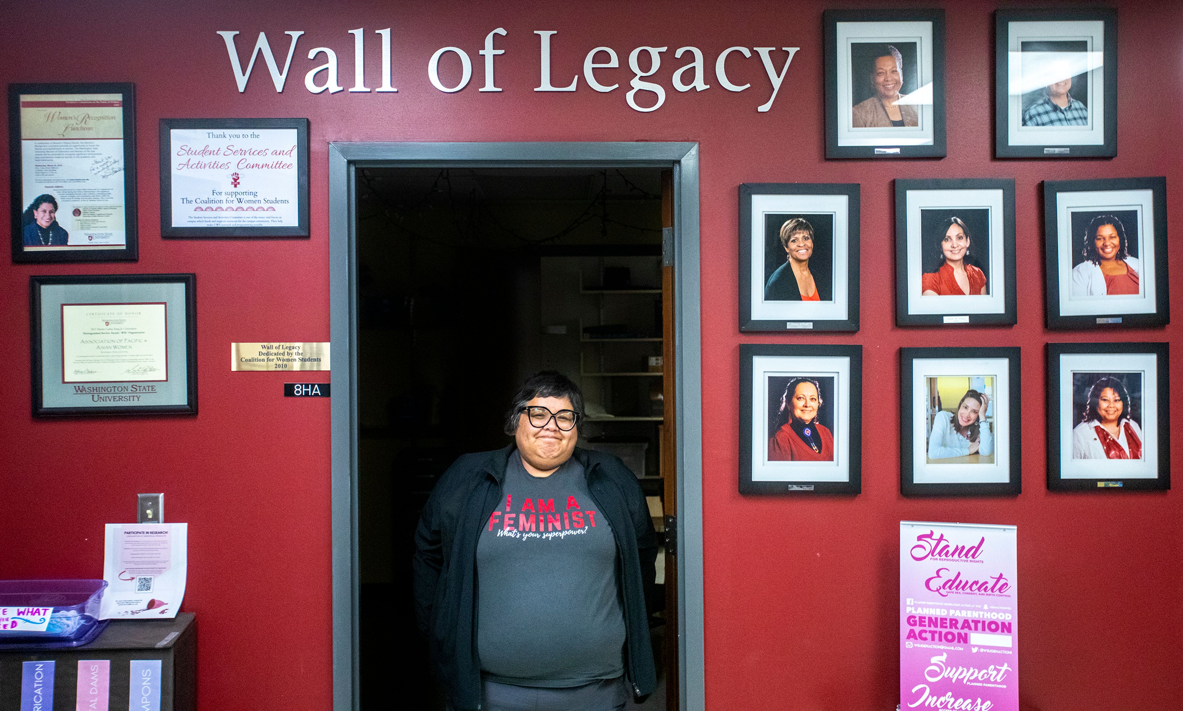 Amy Sharp, director of the Washington State University Women’s Center, stands in a doorway next to the Wall of Legacy made up of pictures of faculty that have helped the students at the center, on Wednesday, Aug. 3.