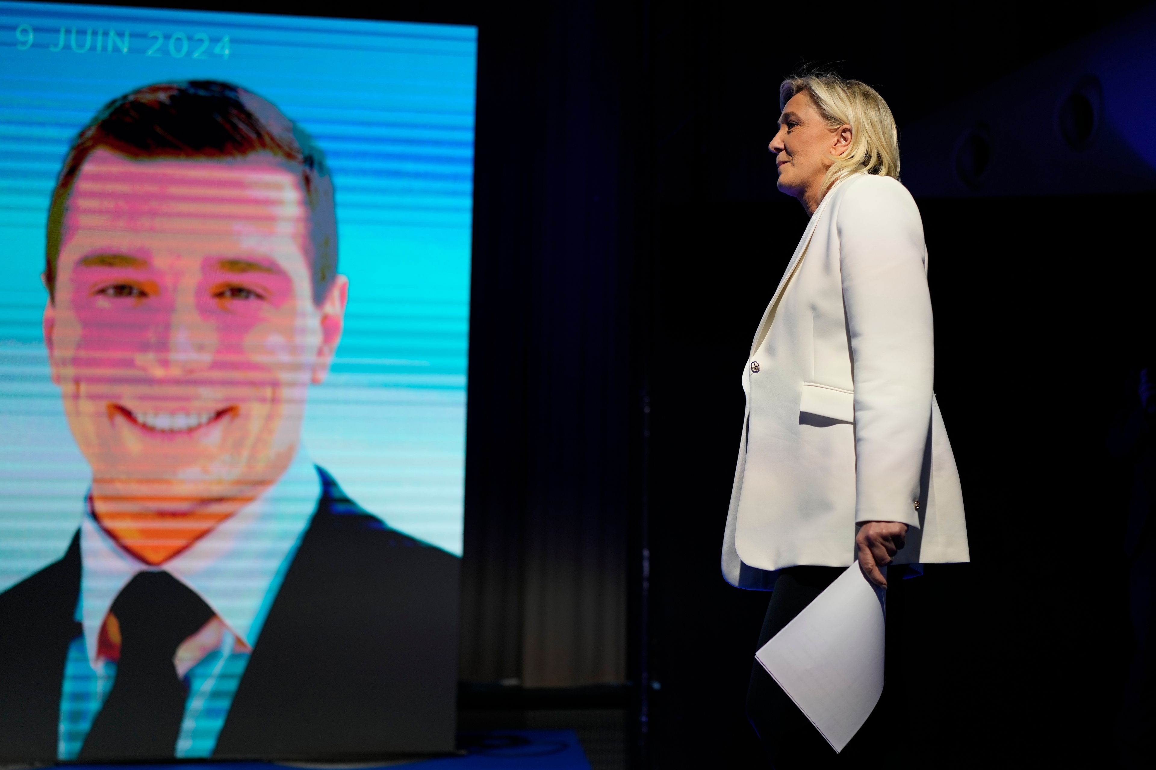 French far-right leader Marine Le Pen walks past a screen showing the president of the French far-right National Rally Jordan Bardella at the party election night headquarters after French President Emanuel Macron announced he dissolves National Assembly and calls new legislative election after defeat in EU vote, Sunday, June 9, 2024 in Paris. First projected results from France put far-right National Rally party well ahead in EU elections, according to French opinion poll institutes.