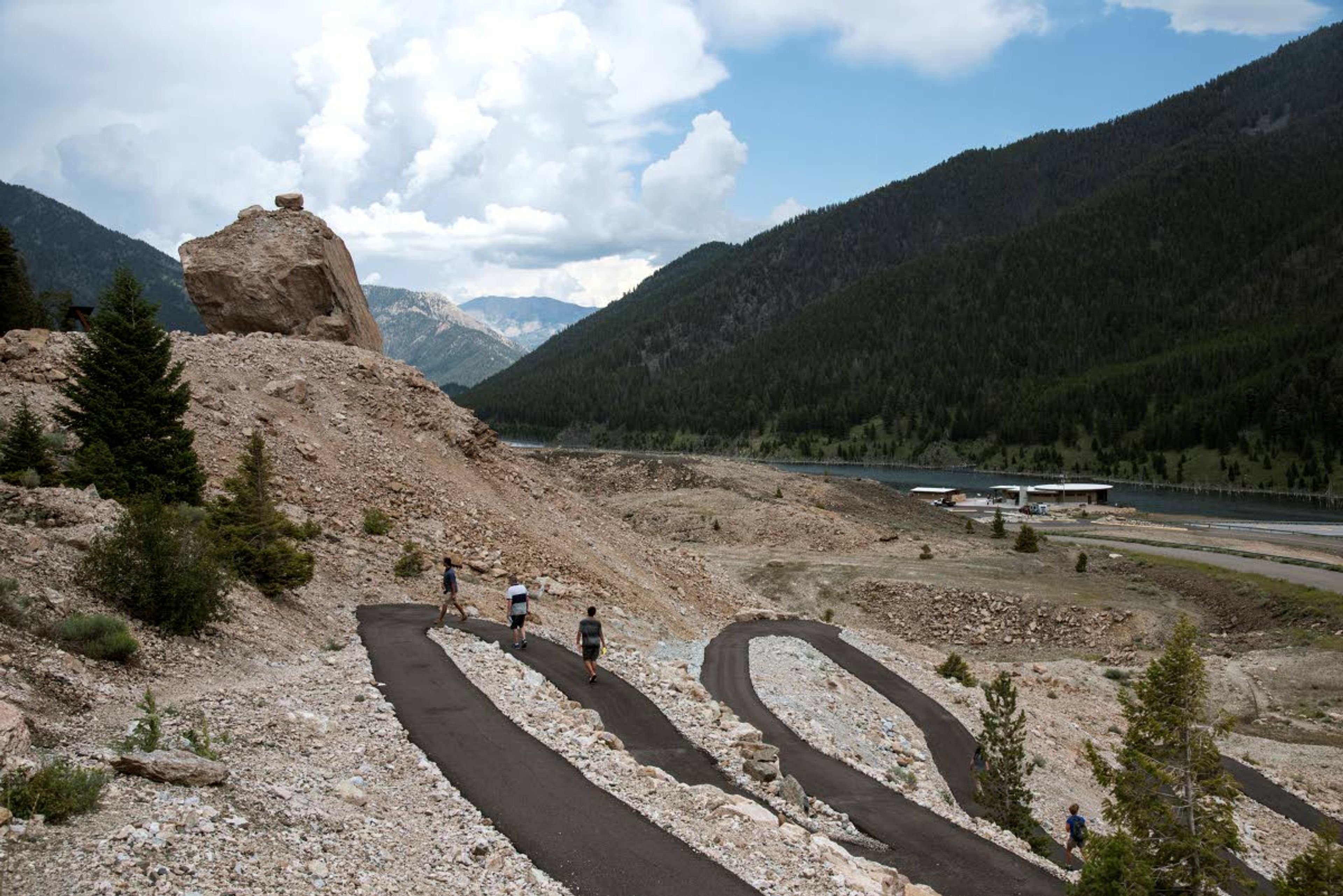 Visitors walk up a trail to visit Memorial and Sister Boulders. In the twenty second landslide, 6-million-pounds of rock and debris travelled half a mile to rest on the opposite side of the valley.An earthquake had disrupted the full-moon night of Aug. 17, 1959, turning it chaotic and terrifying. The quake had a magnitude of 7.3, and it remains the largest to hit the region. The landslide also stopped the river. The water backed up and spread out, turning a swath of canyon into an ominous lake. (Rachel Leathe/Bozeman Daily Chronicle via AP)