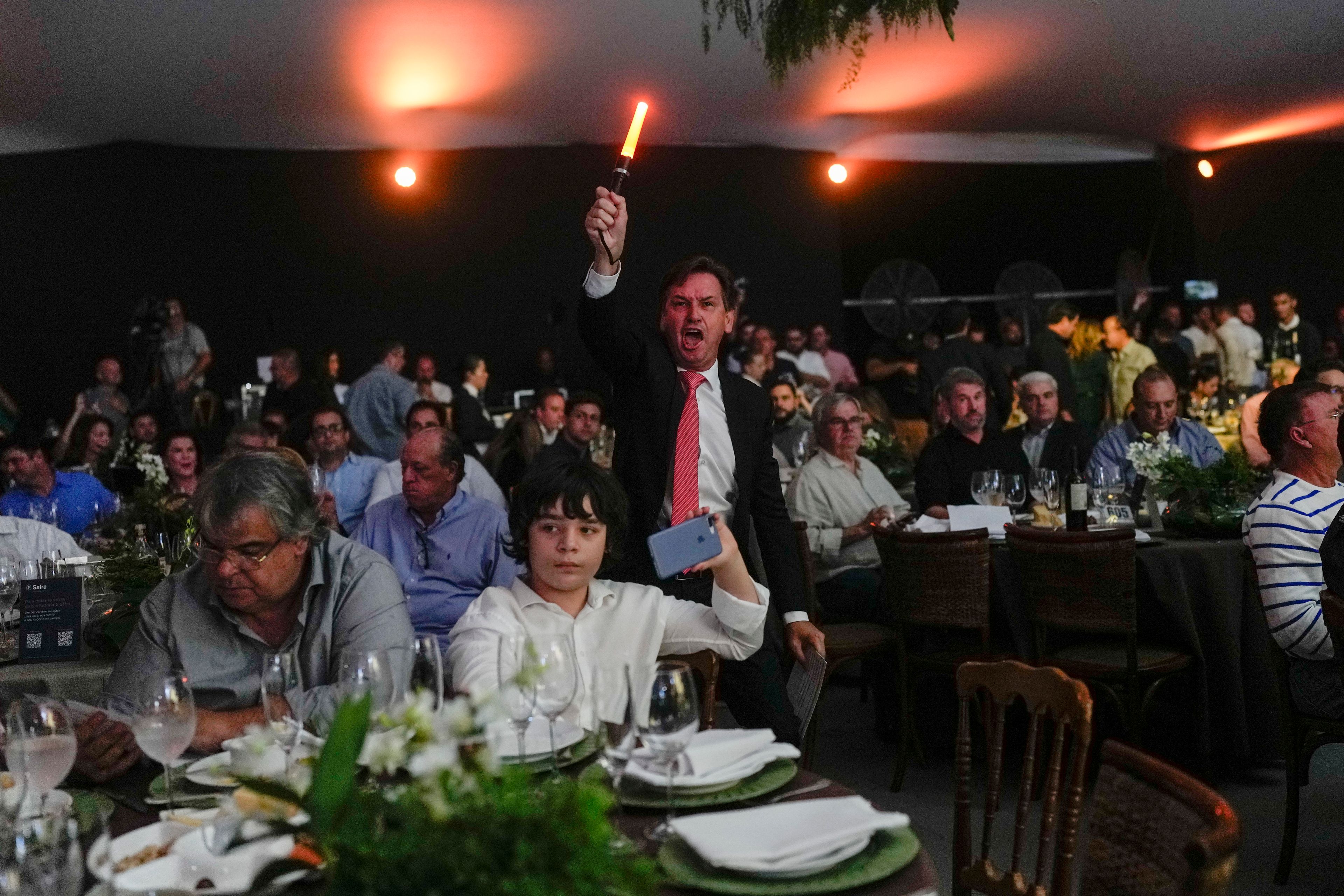 A spotter waves a light stick to signal receipt of a new bid at the Elo de Raça auction in Uberaba, Minas Gerais state, Brazil, Sunday, April 28, 2024. The Elo de Raça is the most prestigious auction taking place on the sidelines of the annual ExpoZebu, which bills itself as the world’s biggest Zebu fair.