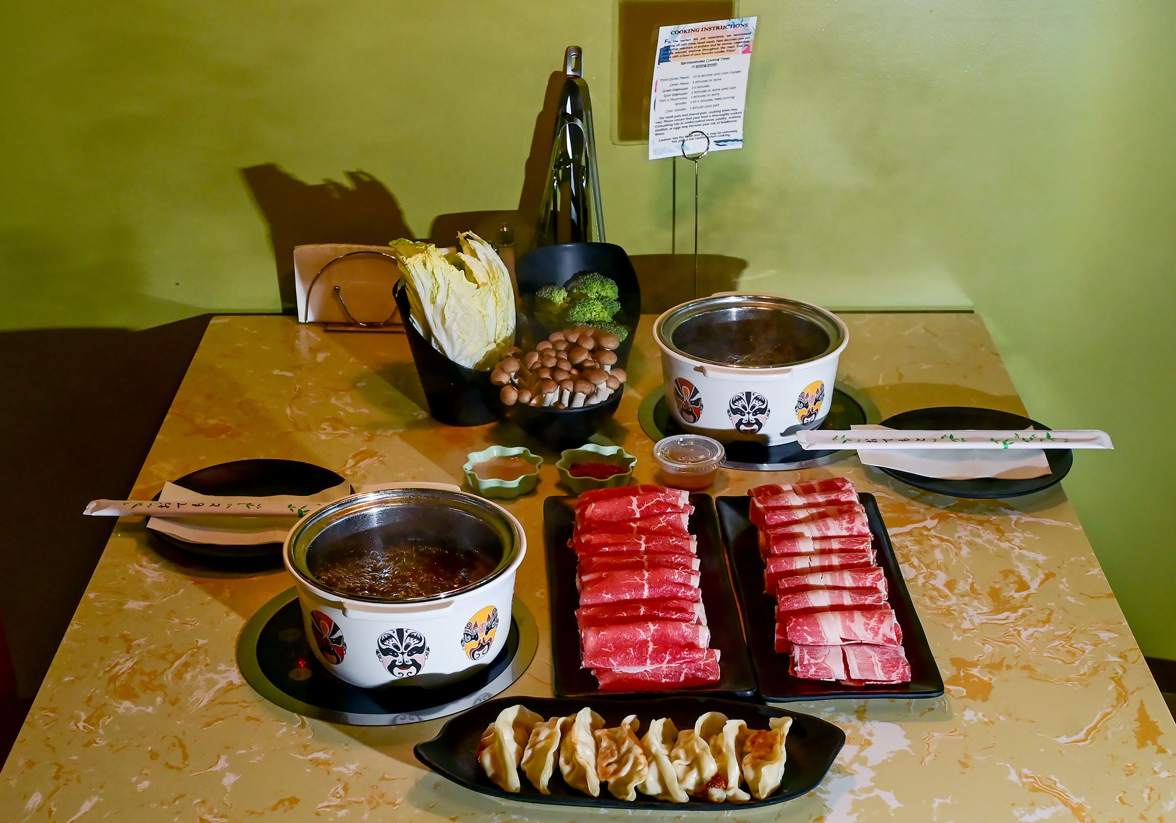 A table is set for two with individual broths including mushroom, left, and hot and spicy, a selection of vegetables including Napa cabbage, broccoli and Shimeji mushrooms, a selection of meats including sirloin slices and marbled beef, right, chicken potstickers and house dipping sauces and spices at Everhot Hot Pot on Wednesday.