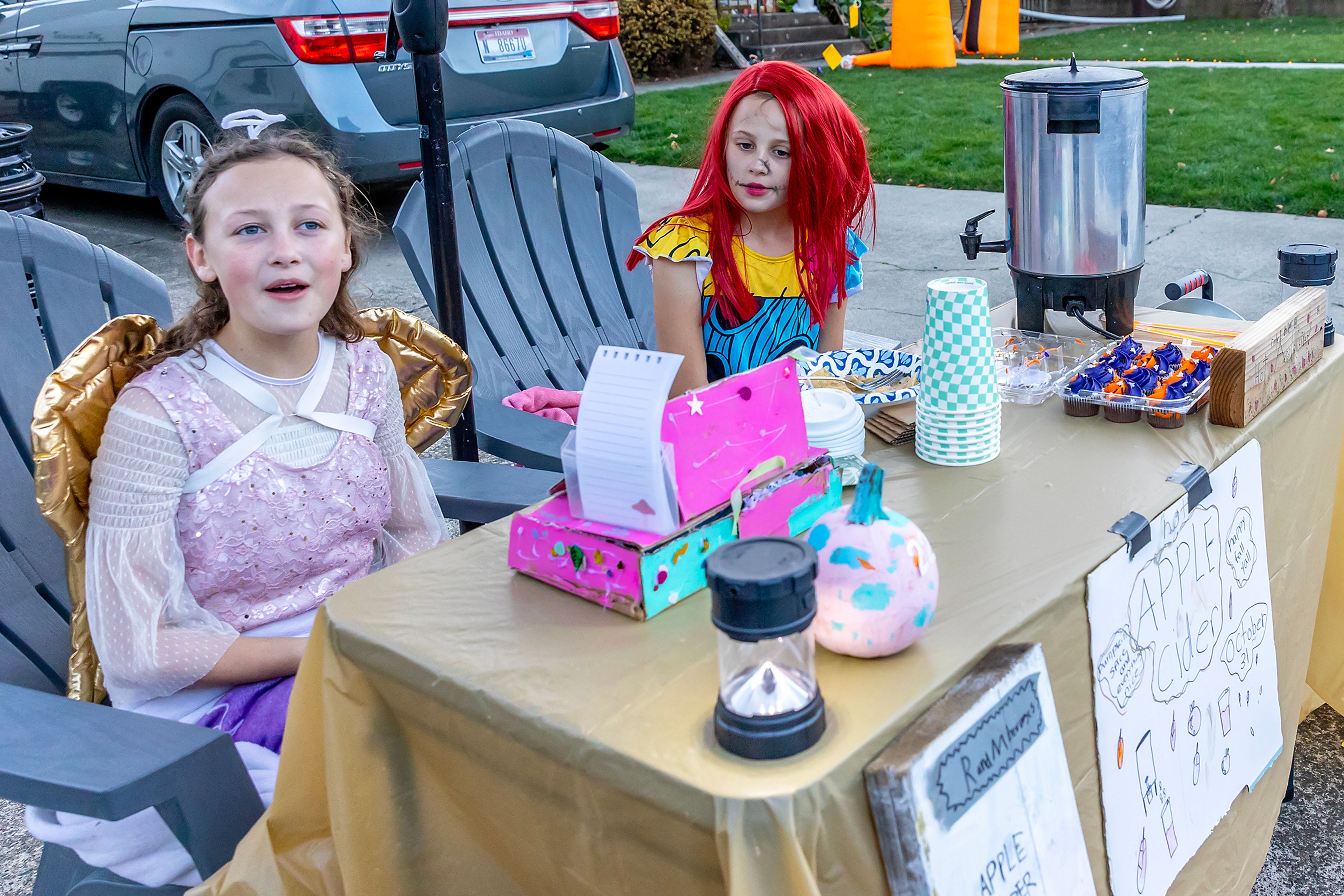 Ruby Royce, dressed as an angel, and Mabel Royce, dressed as Sally from "The Nightmare Before Christmas," sell apple cider, hot coco and water Thursday in the Sunset Drive neighborhood in Lewiston.