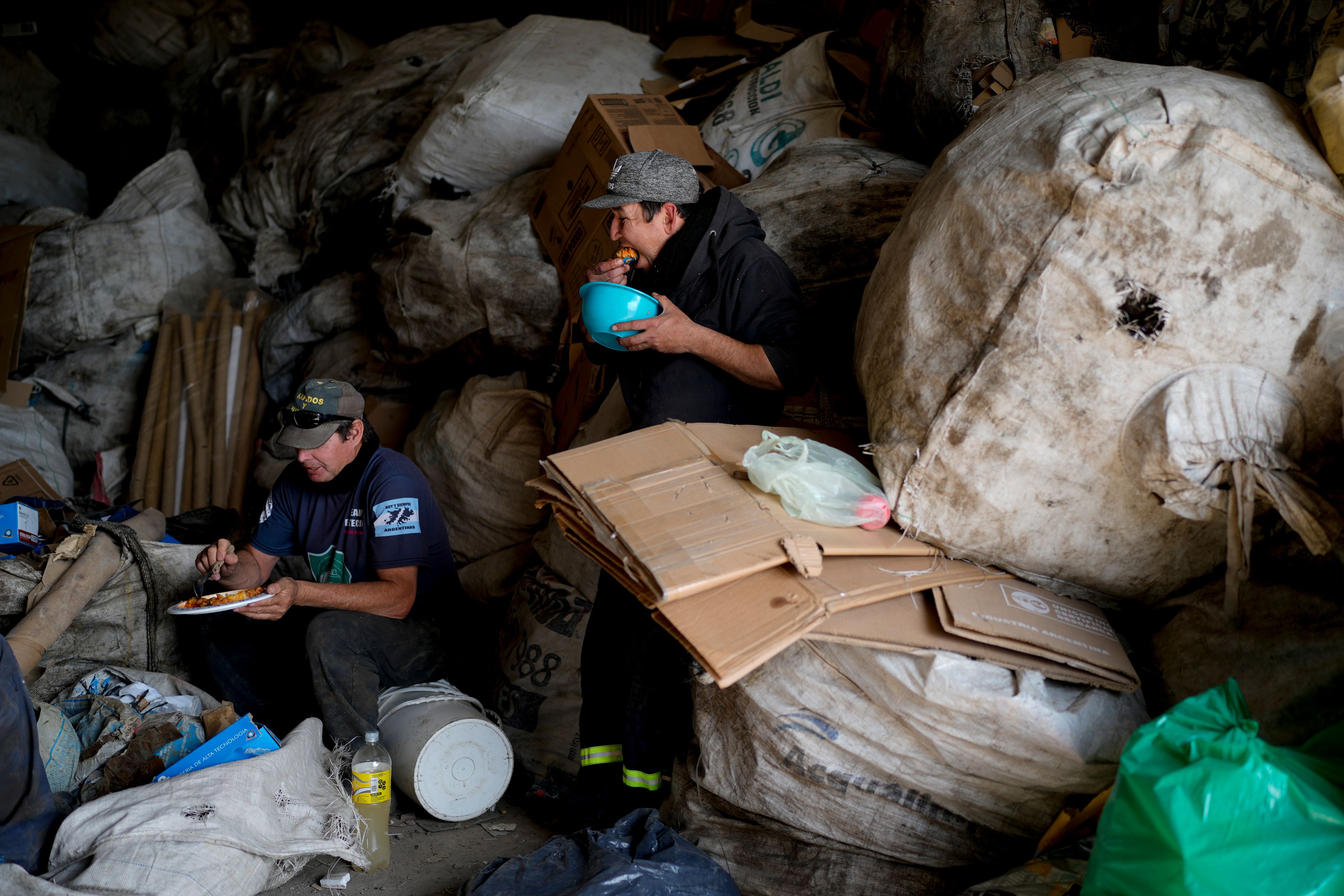 Trash pickers Jose Oman Toledo and Hernan Cardozo eat lunch after cooking for a large group of fellow workers at the recycling plant where they retrieve sellable items in Lujan, Argentina, Thursday, Aug. 29, 2024. (AP Photo/Natacha Pisarenko)