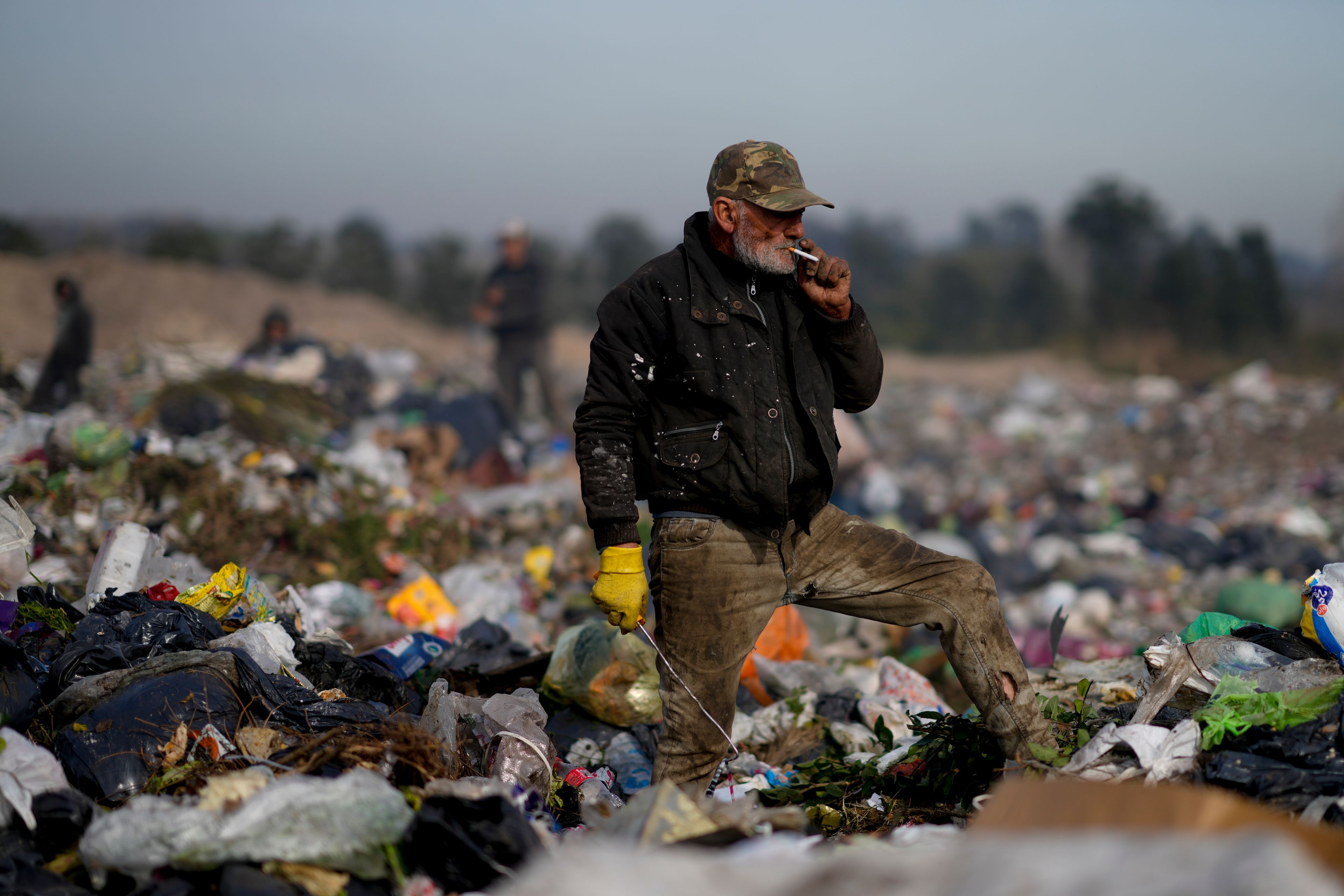 An elderly man pauses to smoke a cigarette as he sifts through garbage at a landfill in search of materials to sell in Lujan, Argentina, Thursday, Aug. 29, 2024. (AP Photo/Natacha Pisarenko)