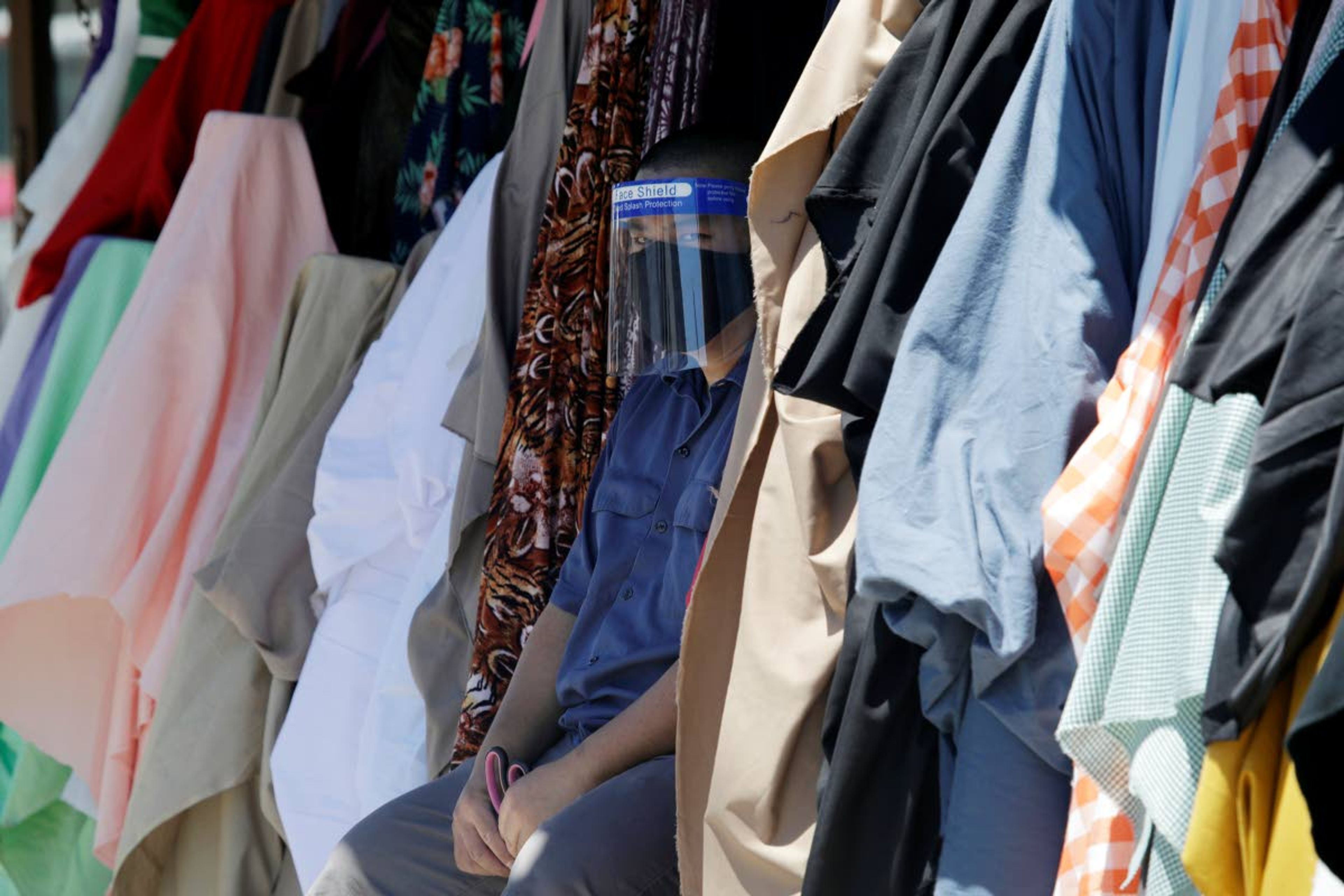 A merchant wears a face shield while selling textiles on the street amid the COVID-19 pandemic Wednesday, May 6, 2020, in Los Angeles. (AP Photo/Marcio Jose Sanchez)