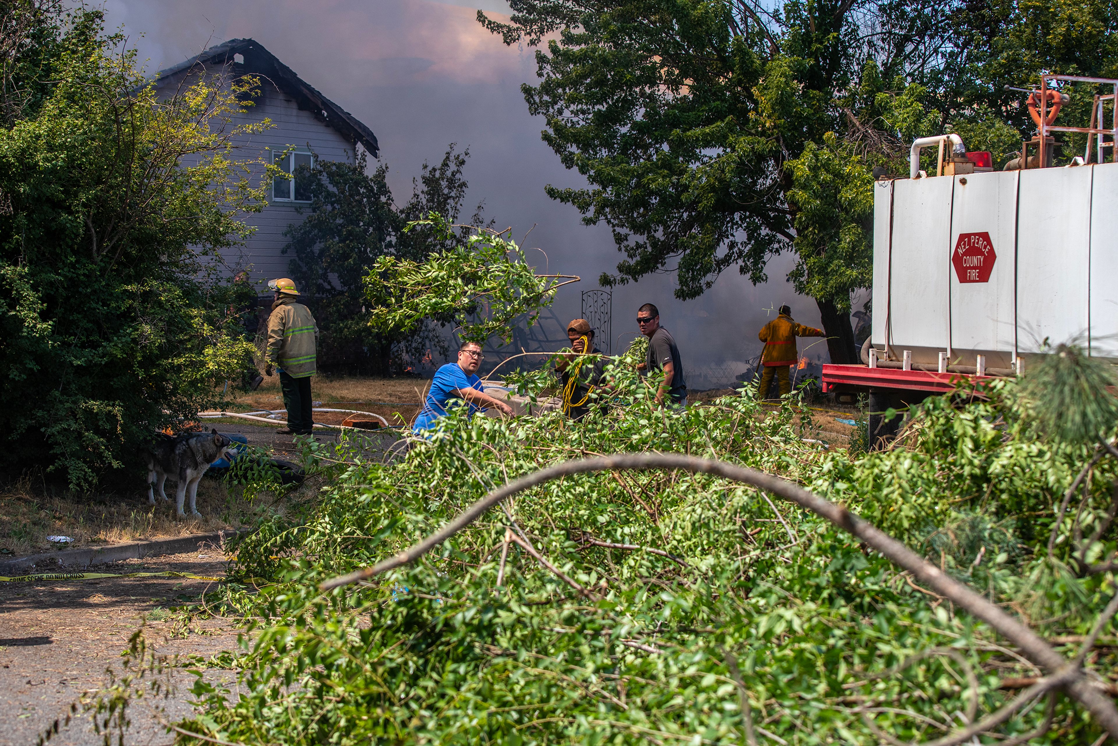 People throw cut branches into a pile to keep the fire from spreading at the scene of a structure fire Friday on Lolo Street in Lapwai.