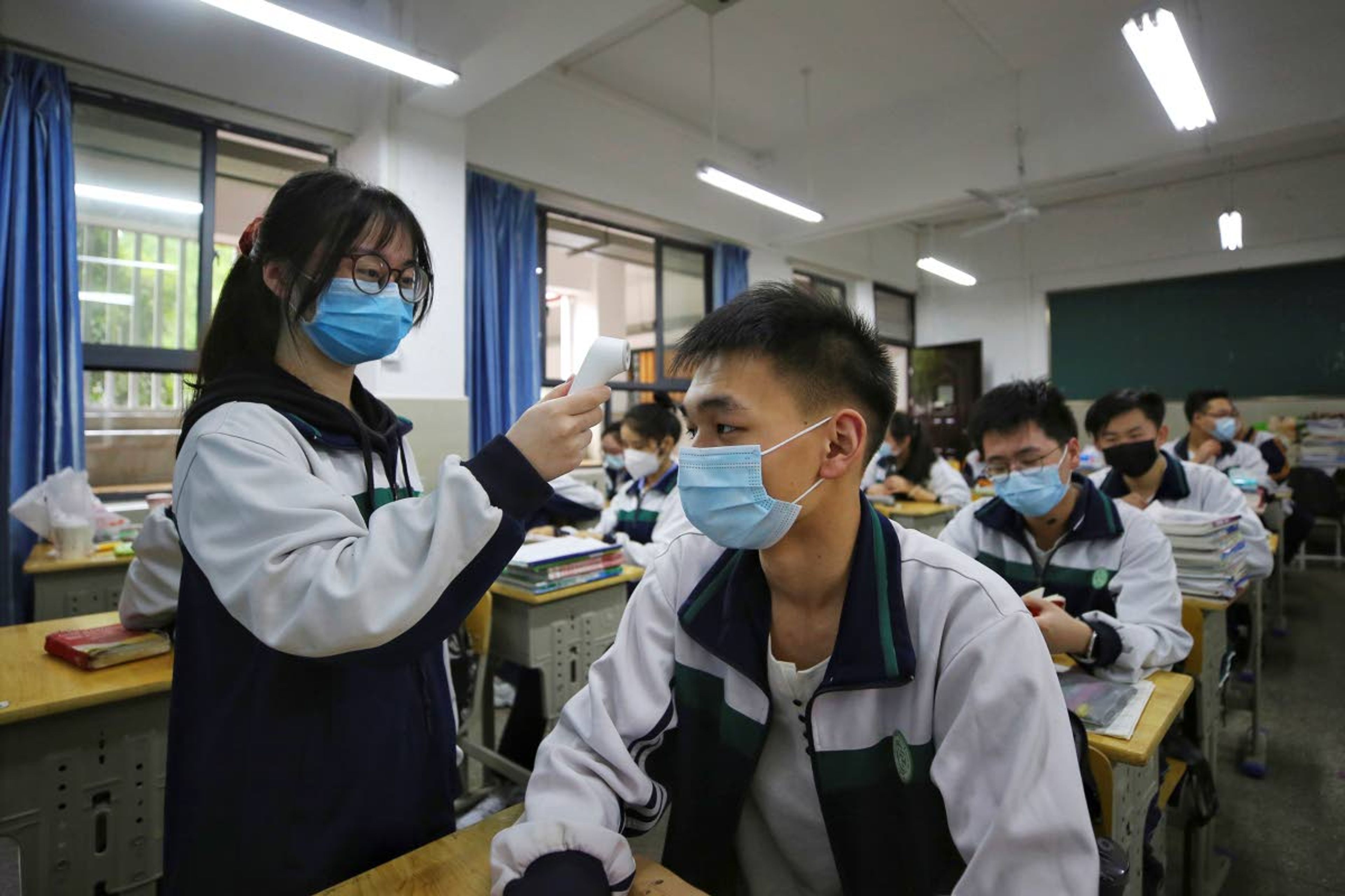 A female student wearing a protective face mask to help curb the spread of the new coronavirus checks temperature of her classmates at a high school in Wuhan in central China's Hubei province, Wednesday, May 6, 2020. Senior students returned to classes on Wednesday in the central Chinese city of Wuhan, the epicenter of the coronavirus pandemic, after no new cases or deaths were reported from the outbreak that had prompted a 76-day quarantine in the city of 11 million. (Chinatopix via AP)