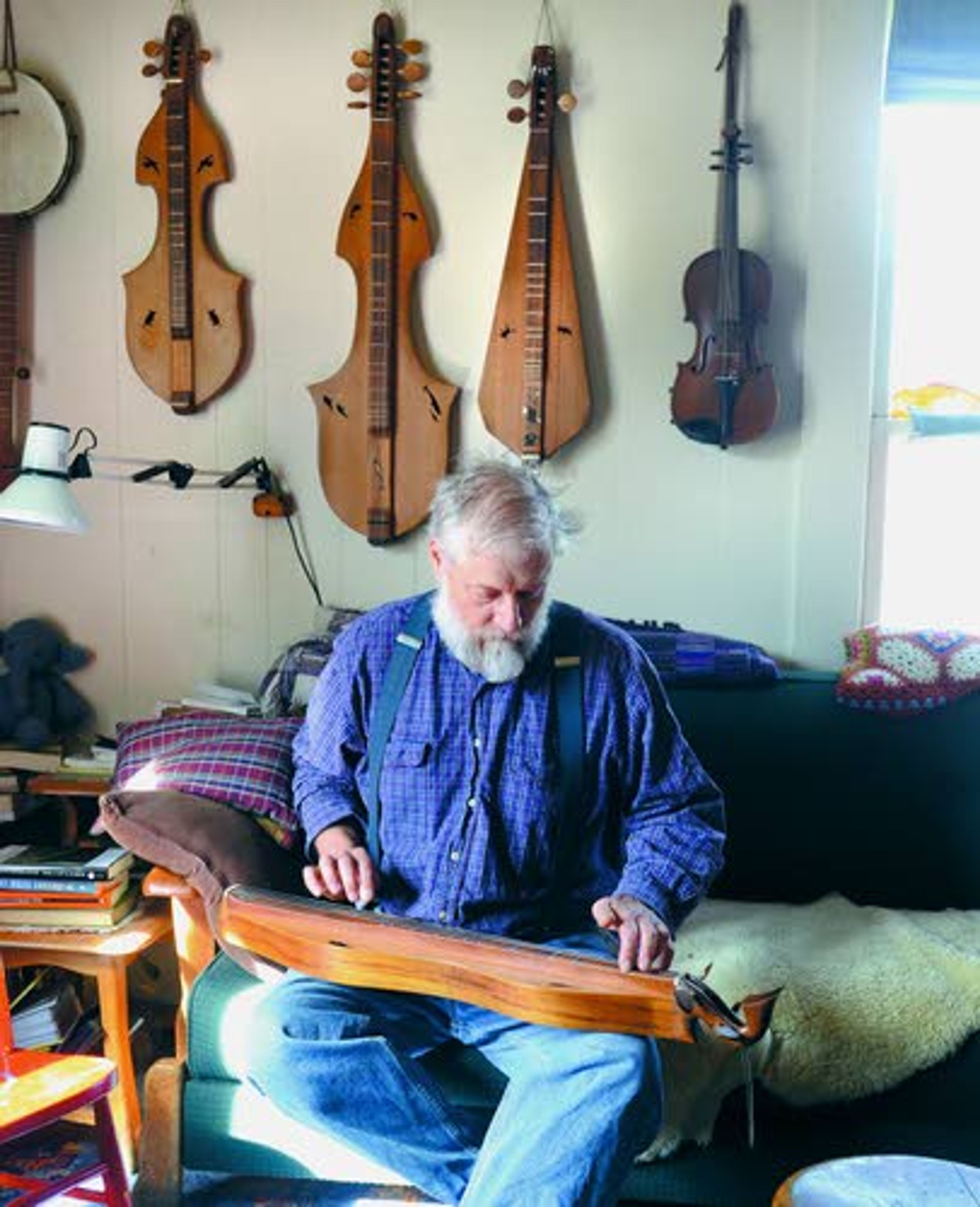 Tribune/Barry KoughJohn Elwood tries one of his many handmade dulcimers. He says he can teach the basics of playing one to a beginner in ten minutes.