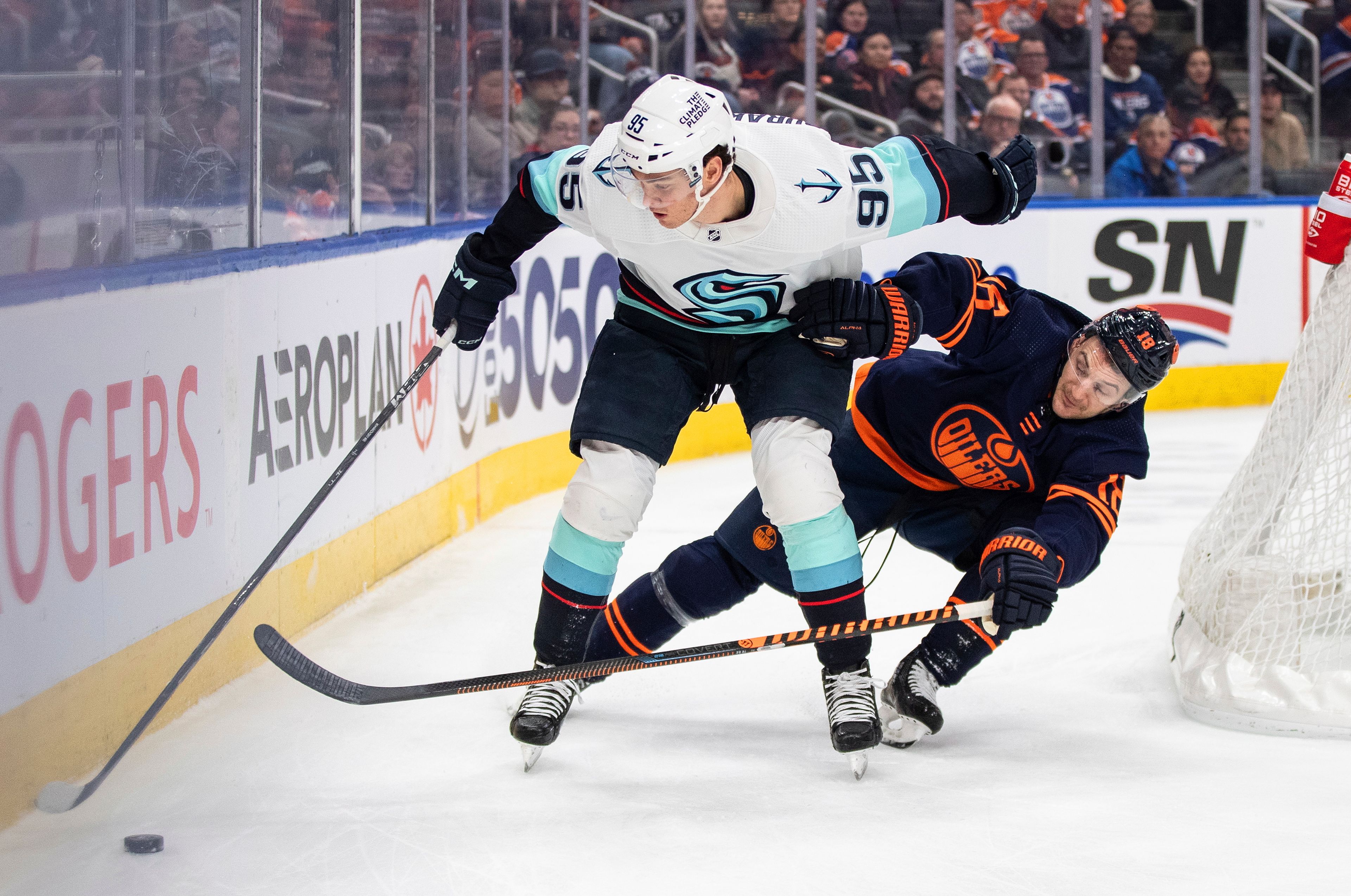 Seattle Kraken's Andre Burakovsky (95) and Edmonton Oilers' Zach Hyman (18) reach for the puck during the first period of an NHL hockey game Tuesday, Jan. 17, 2023, in Edmonton, Alberta. (Jason Franson/The Canadian Press via AP)