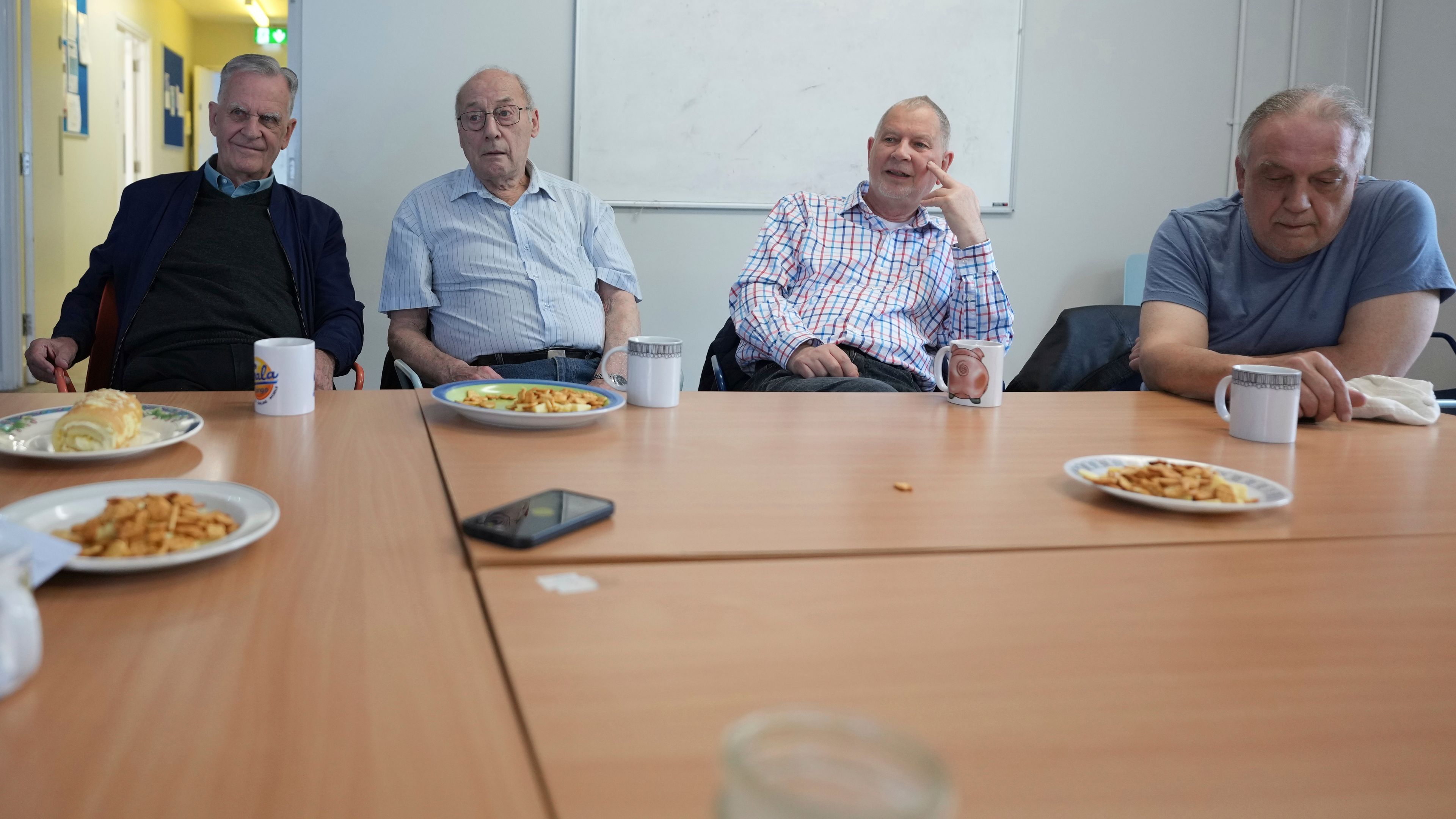 Alan Tucker, second right, listens at the weekly lunch meeting of some 20 retired men at the Tredegar community centre in Bow, in east London, Thursday, May 16, 2024. Passing around plates of cheese and crackers and slices of crème cake, they drank steaming coffee and tea. What they wanted was a chance to vent about the problems facing Britain and the fact that no one is listening to them as the country prepares for an election later this year. (AP Photo/Alastair Grant)