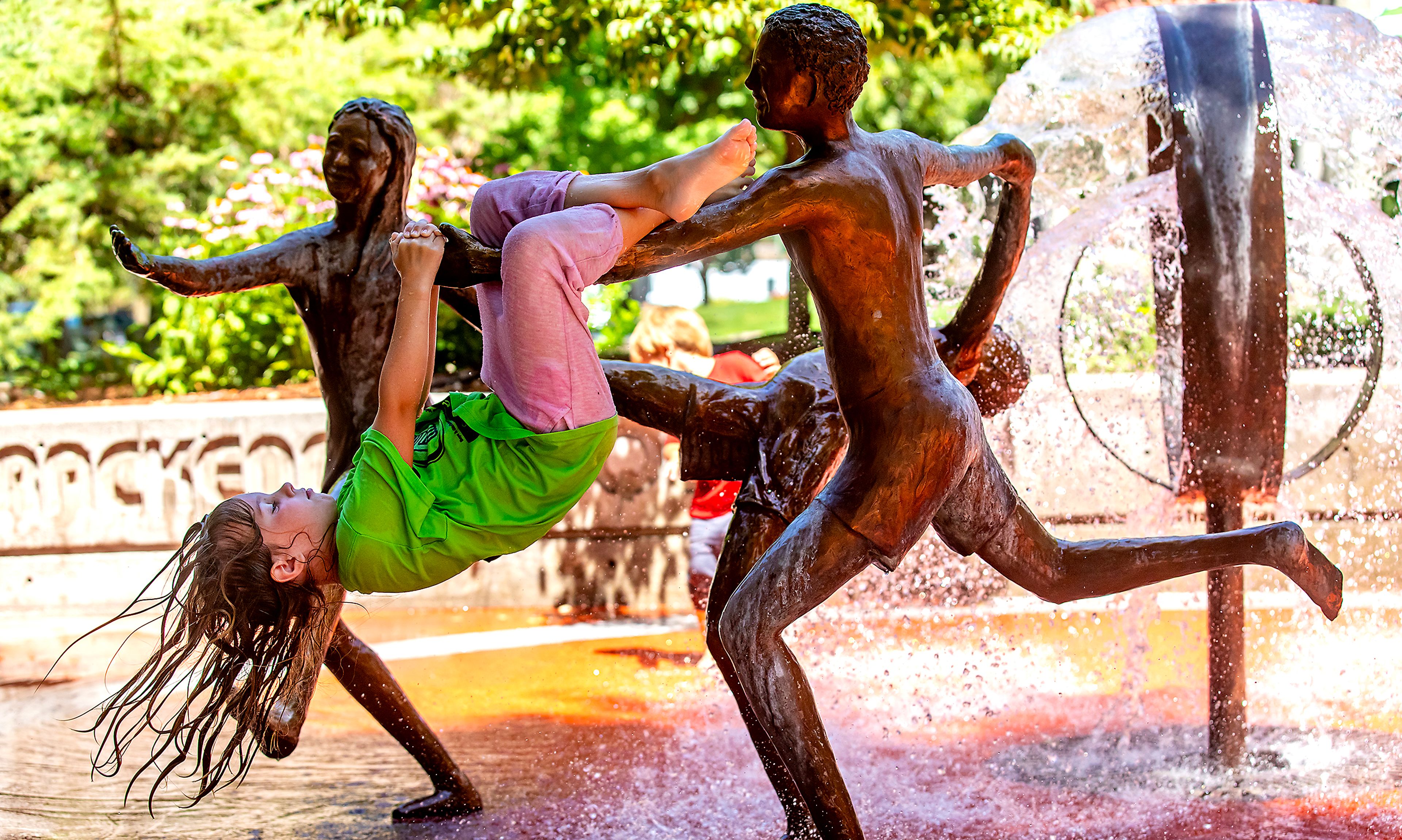 Fiona Karlin, 7, of Lewiston, hangs off the statue at Brackenbury Square as she and her brother play in the fountain Friday in Lewiston.