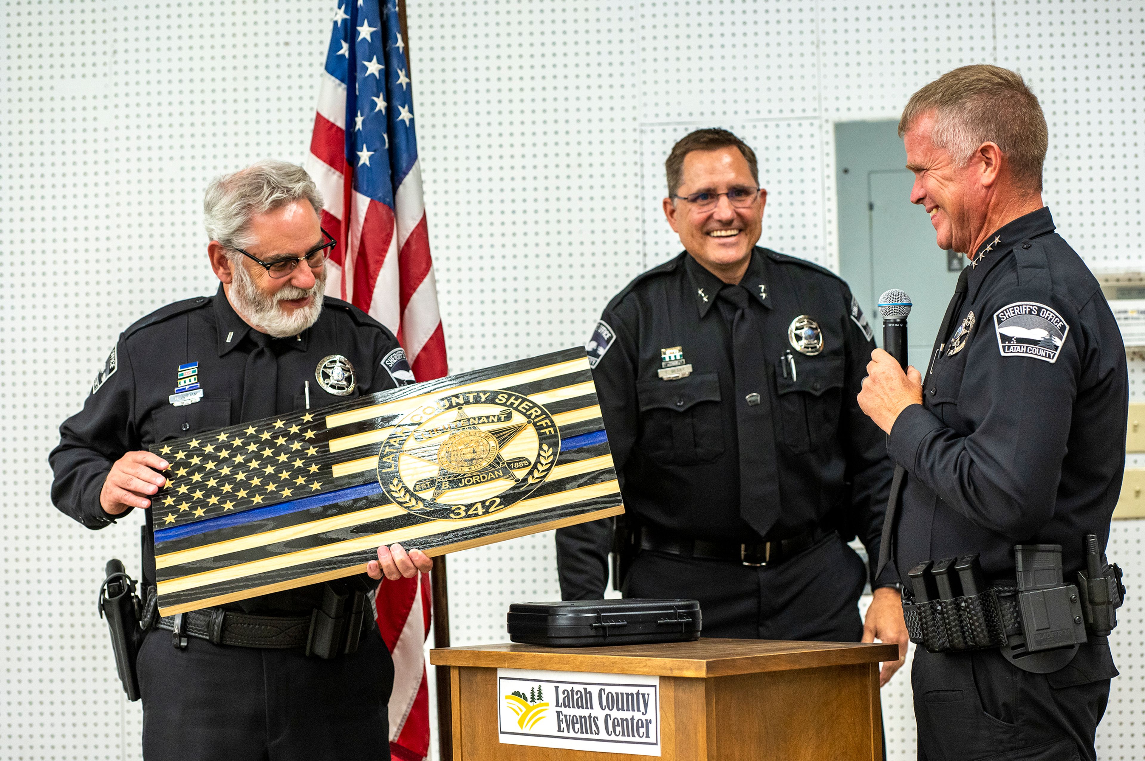 Lt. Brannon Jordan is presented Thursday with a wood carved American flag with his badge engraved in it from Chief Deputy Tim Besst, middle, and Sheriff Richie Skiles during Jordan’s retirement party from the Latah County Sheriff’s Office at the Latah County Fair Office in Moscow.