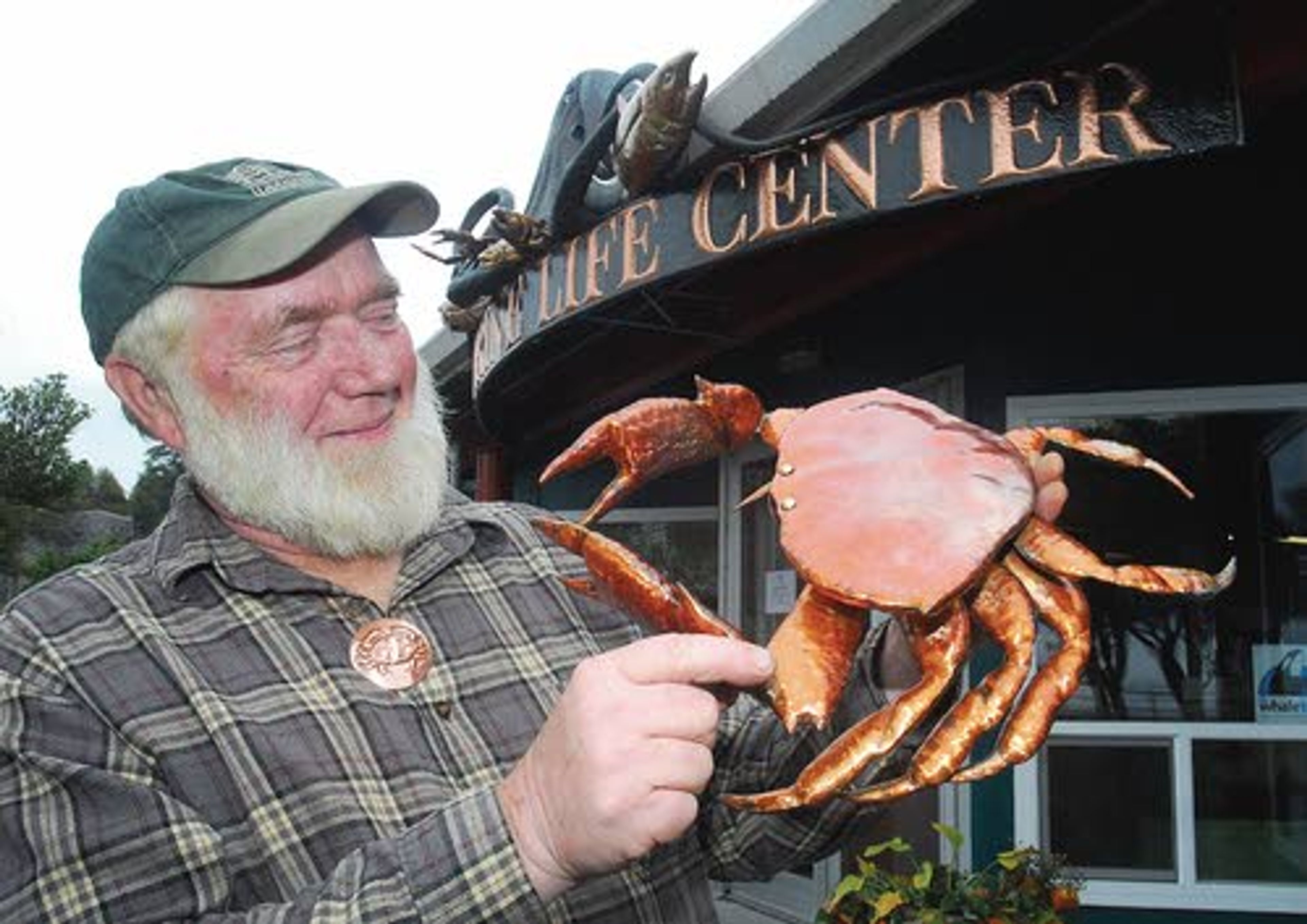 Coopersmith Clark Mundy shows off one of his copper crab sculptures Thursday in Port Angeles, Wash. Mundy is the featured artist at this weekend’s Dungeness Crab & Seafood Festival. Mundy also fashioned the decorative facade of the Feiro Marine Life Center, shown in the background, at Port Angeles City Pier.