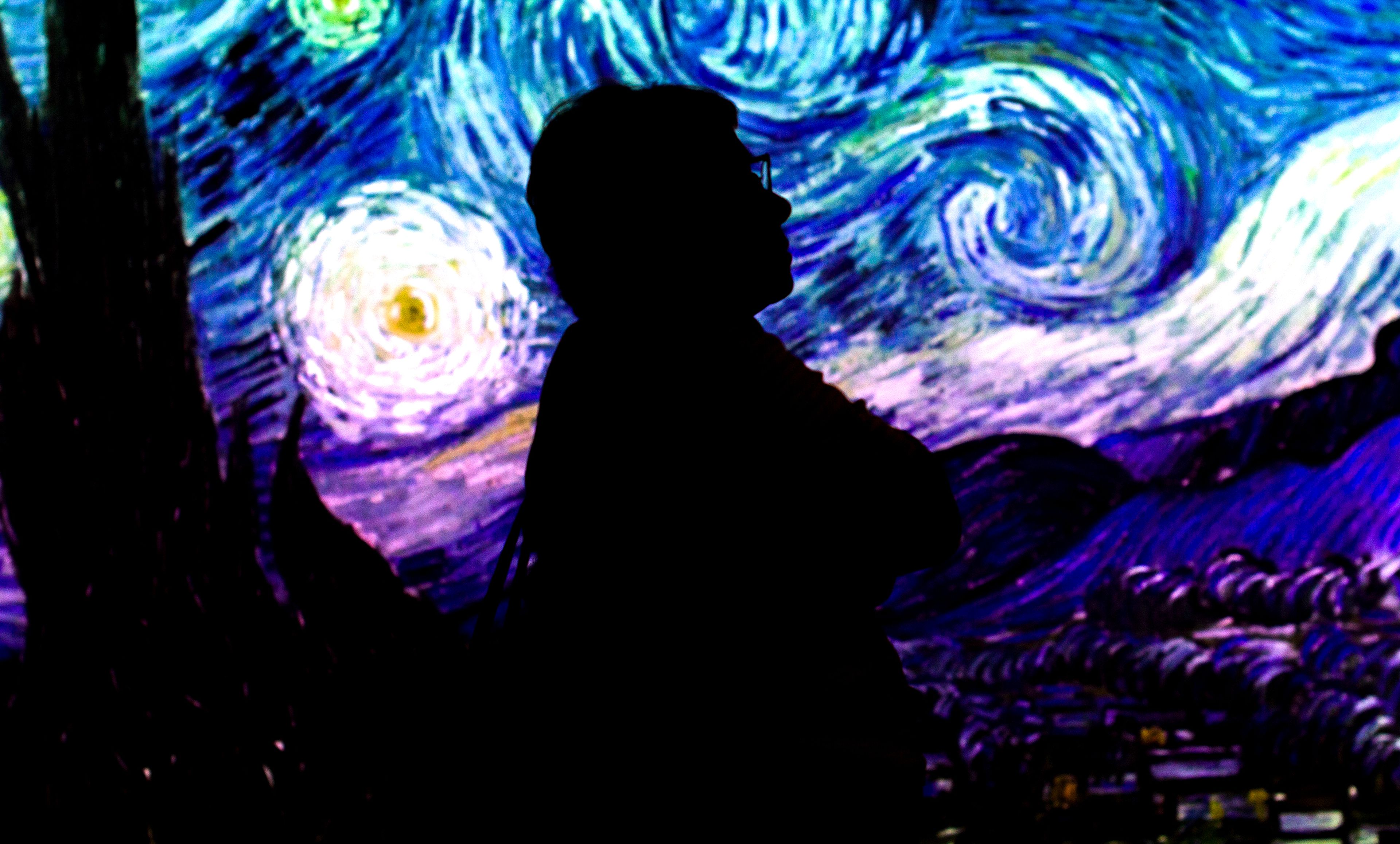 A visitor to the Van Gogh Immersive Experience looks around as the picture “The Starry Night” sits in the background on July 29 in Spokane.