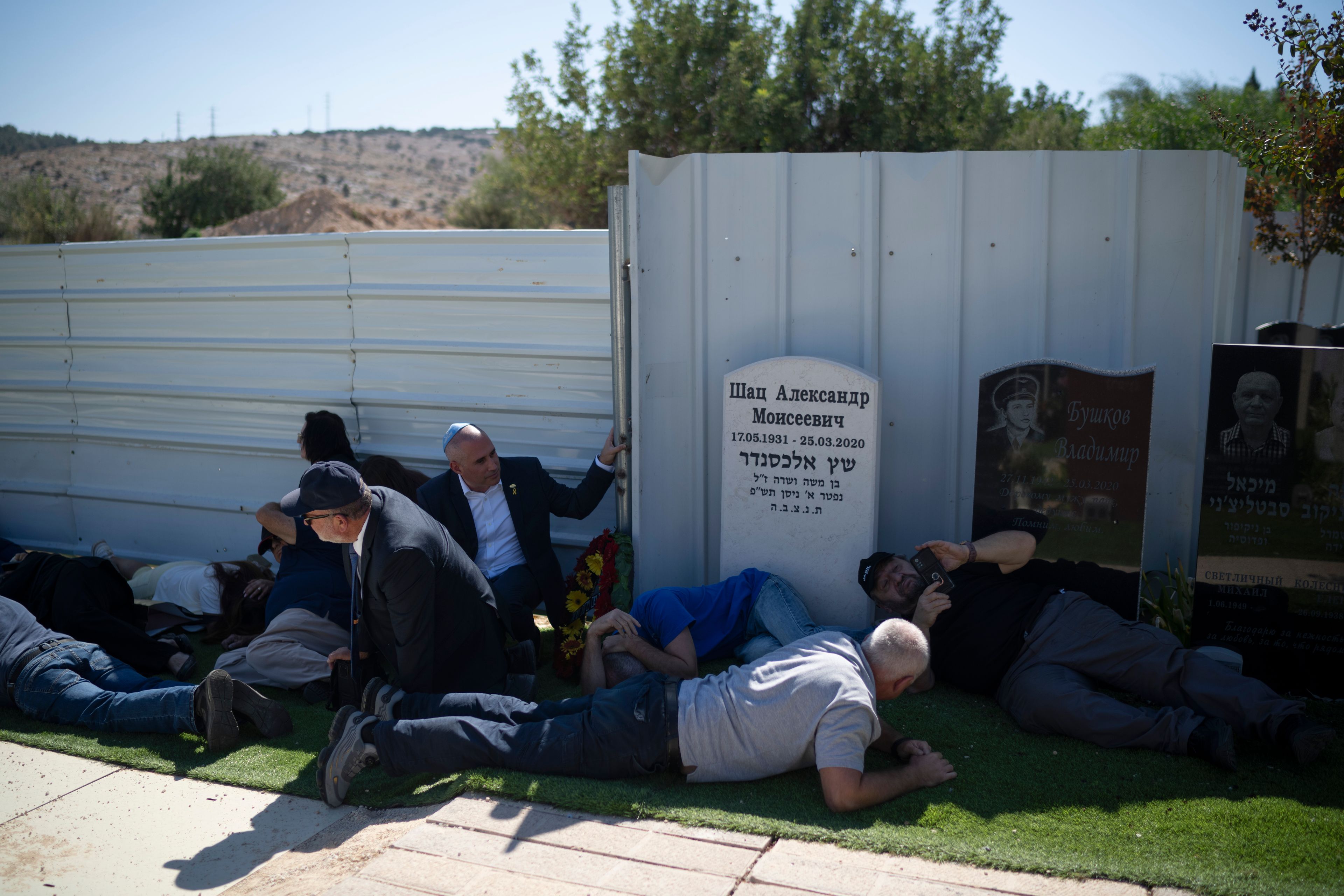 People take cover as a siren warns of incoming rockets during the funeral of Alexei Popov, who was killed during a rocket attack fired from Lebanon last weekend, at the Tel Regev cemetery in the outskirts of Haifa, northern Israel, Monday, Oct. 21, 2024. (AP Photo/Leo Correa)