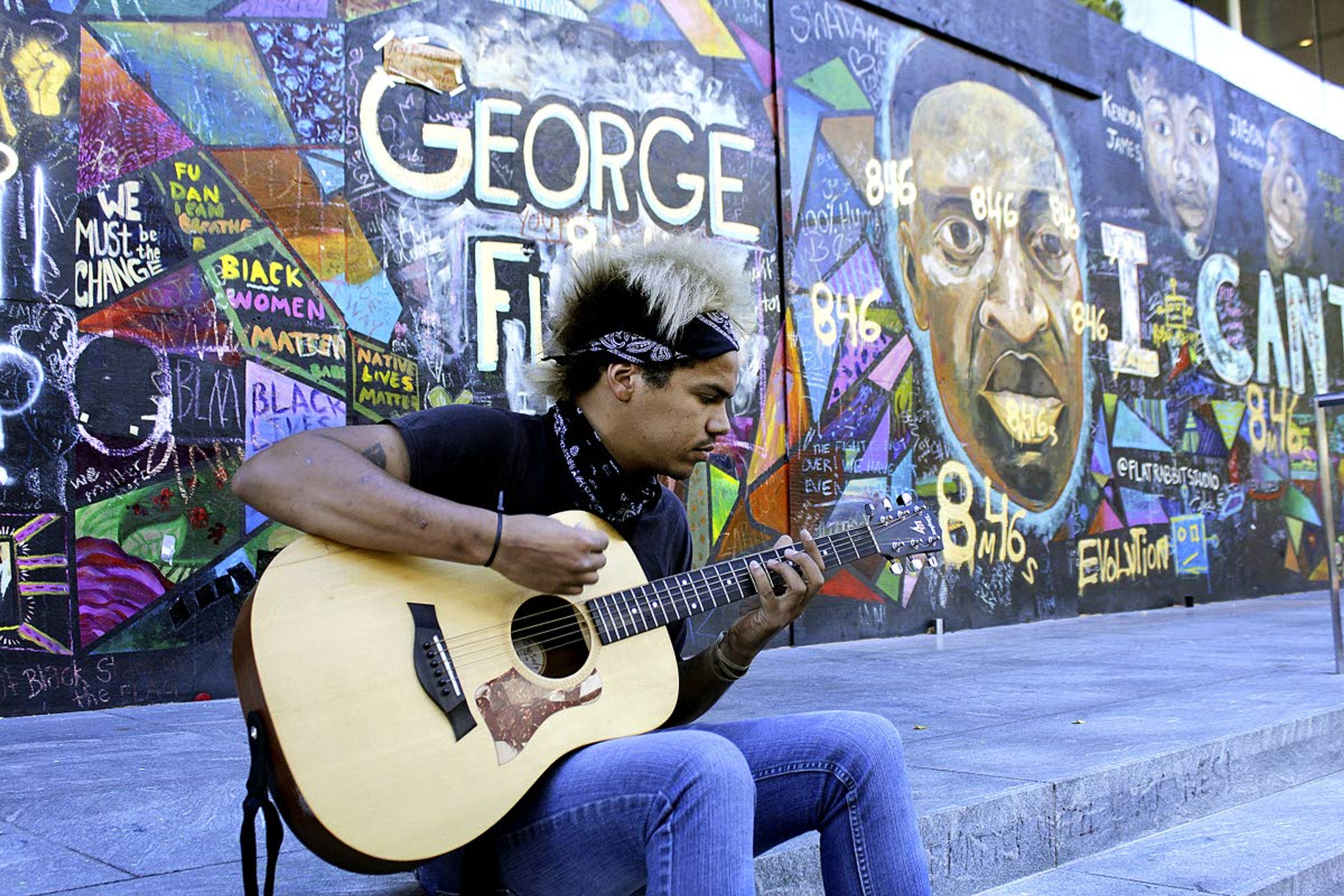 In this photo taken Aug. 27, Shane Braswell, who has protested at least 60 days since late May, spends an afternoon playing acoustic guitar in front of a huge mural of George Floyd in downtown Portland, Ore. The mural, painted by artist Emma Berger is dedicated to Black people killed by police, among them Floyd, who was choked to death during an arrest in Minneapolis earlier this year.