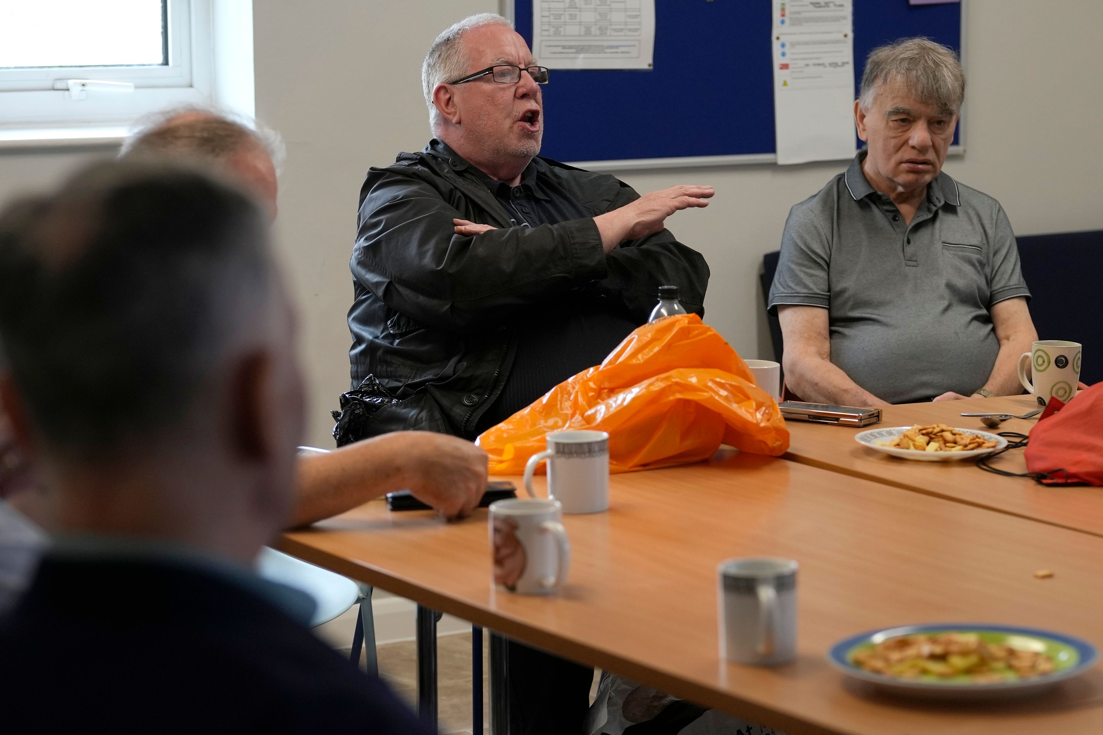 Barrie Stradling, left speaks at the weekly lunch meeting of some 20 retired men at the Tredegar community centre in Bow, in east London, Thursday, May 16, 2024. Passing around plates of cheese and crackers and slices of crème cake, they drank steaming coffee and tea. What they wanted was a chance to vent about the problems facing Britain and the fact that no one is listening to them as the country prepares for an election later this year. (AP Photo/Alastair Grant)