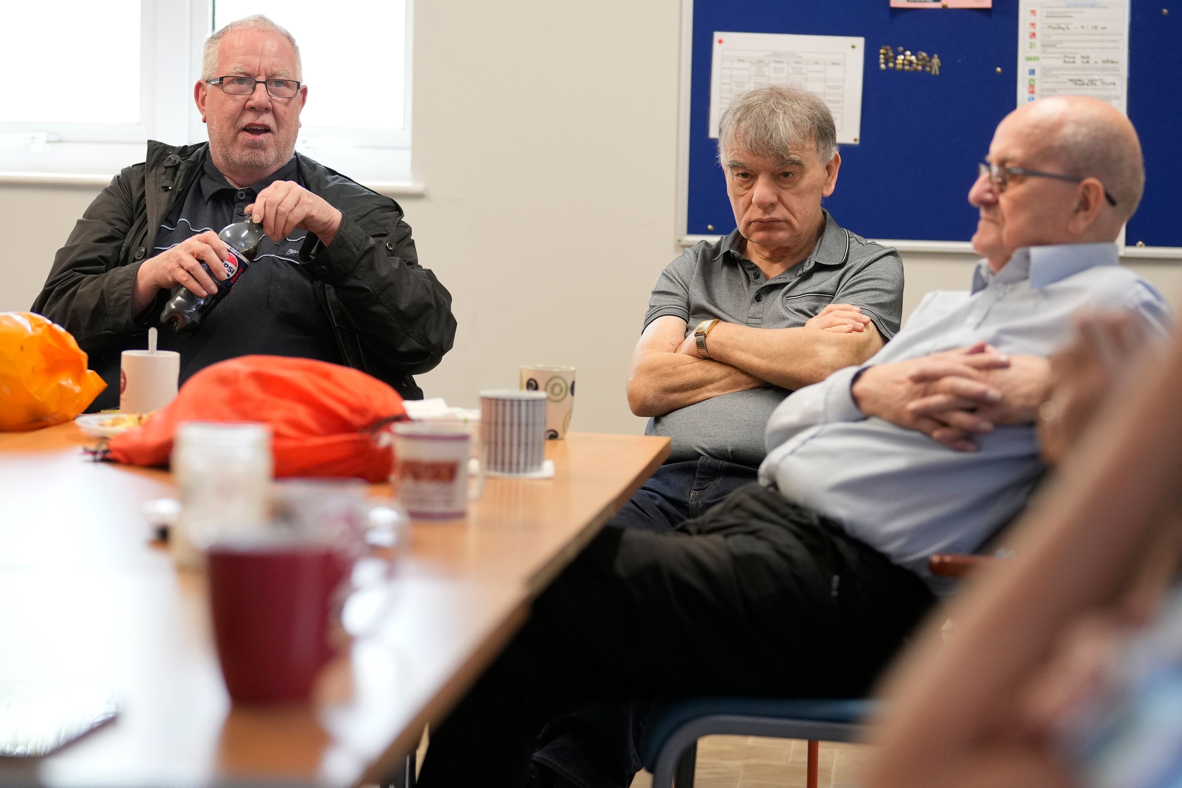 Barrie Stradling, left speaks at the weekly lunch meeting of some 20 retired men at the Tredegar community centre in Bow, in east London, Thursday, May 16, 2024. Passing around plates of cheese and crackers and slices of crème cake, they drank steaming coffee and tea. What they wanted was a chance to vent about the problems facing Britain and the fact that no one is listening to them as the country prepares for an election later this year. (AP Photo/Alastair Grant)