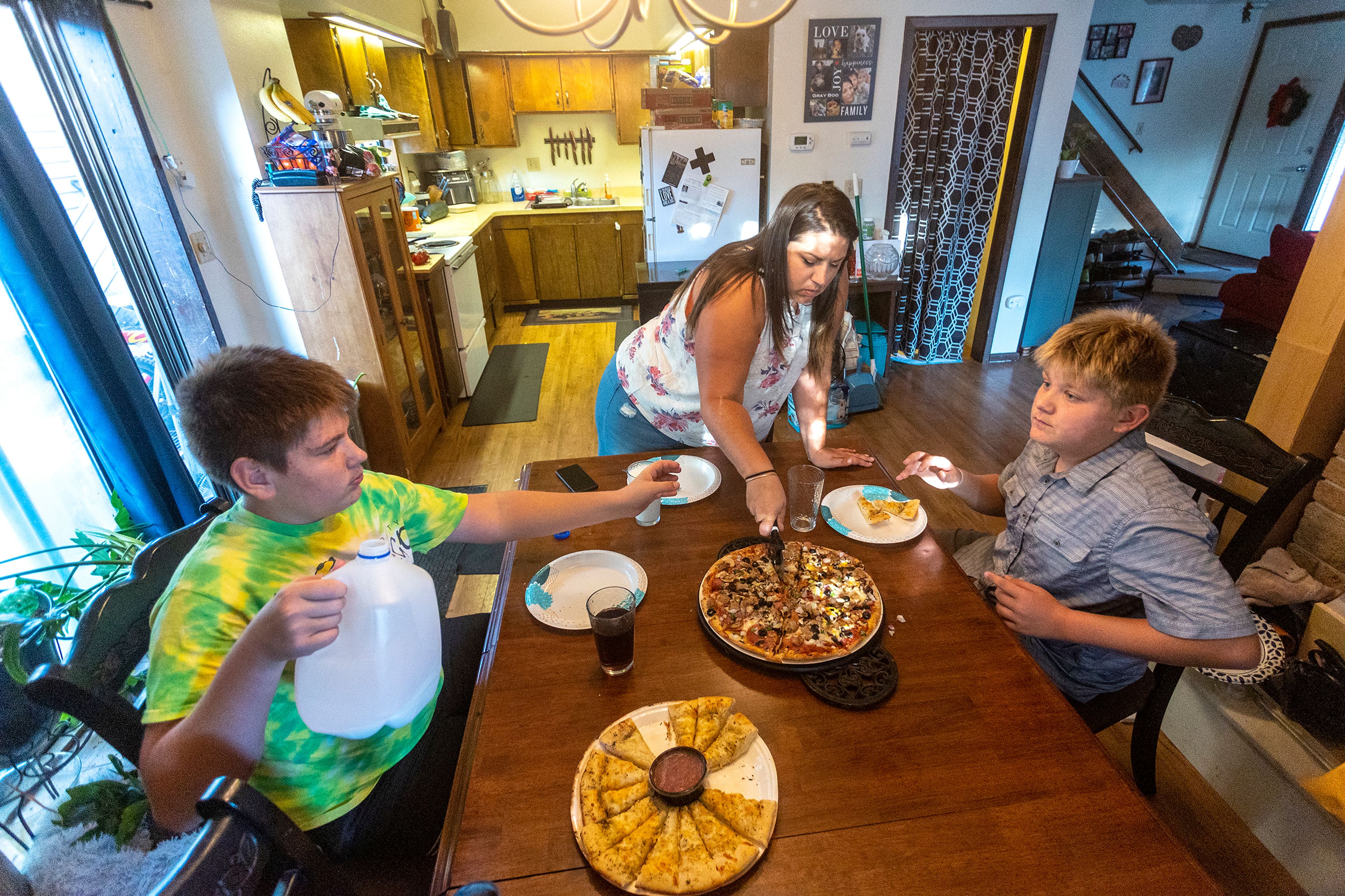 Aimee Martinez cuts up a pizza as her boys Alex Poulsen, left, and Tony Poulsen pour some milk as they sit down for dinner on Friday.