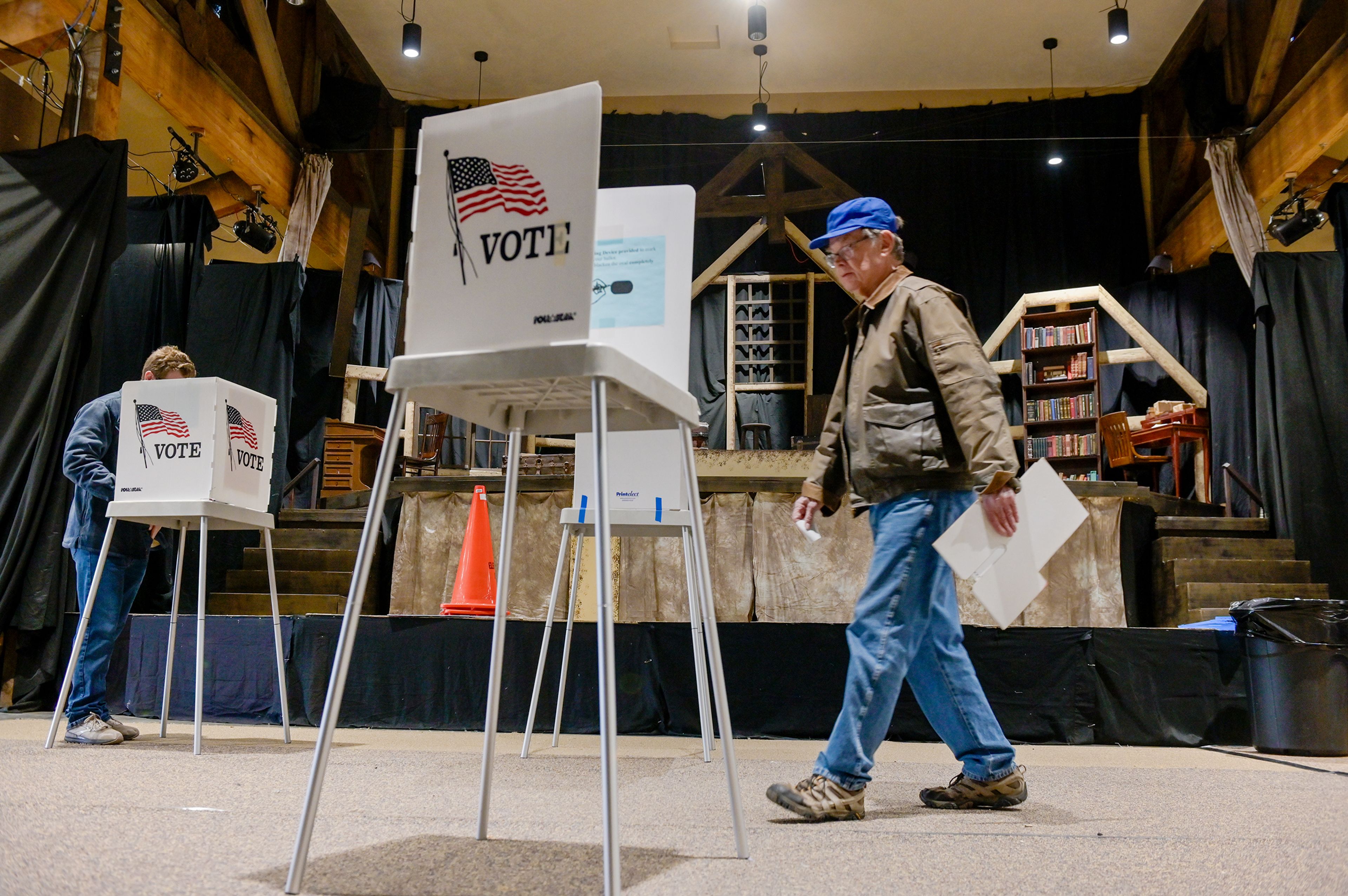 Voters walk by a stage set for a production of “Little Women: The Broadway Musical” to reach their polling booths set up at the Viola Community Center Tuesday in Viola.