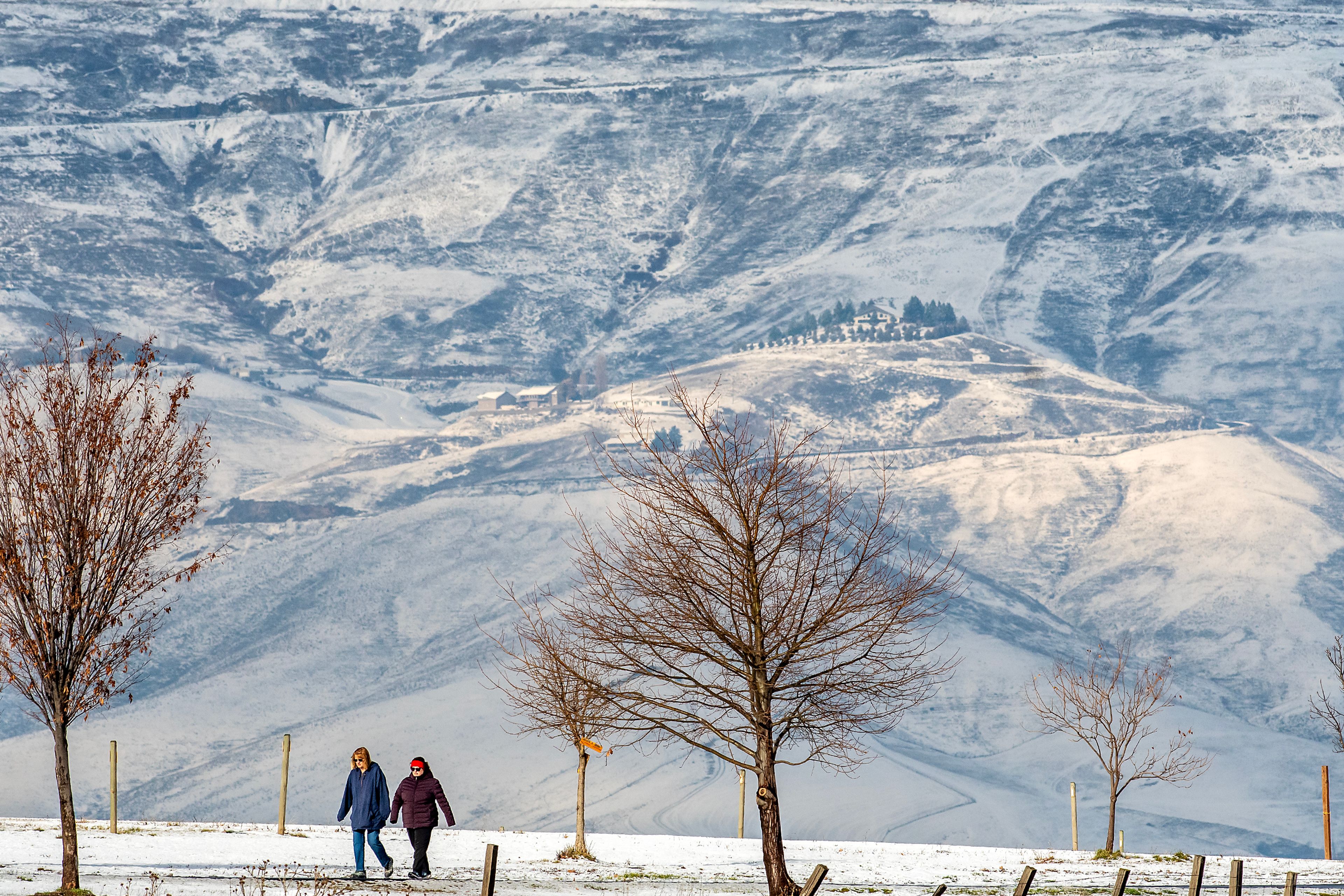 People walk down the trail at Community Park Wednesday in the Lewiston Orchards as snow covers the northern hills.