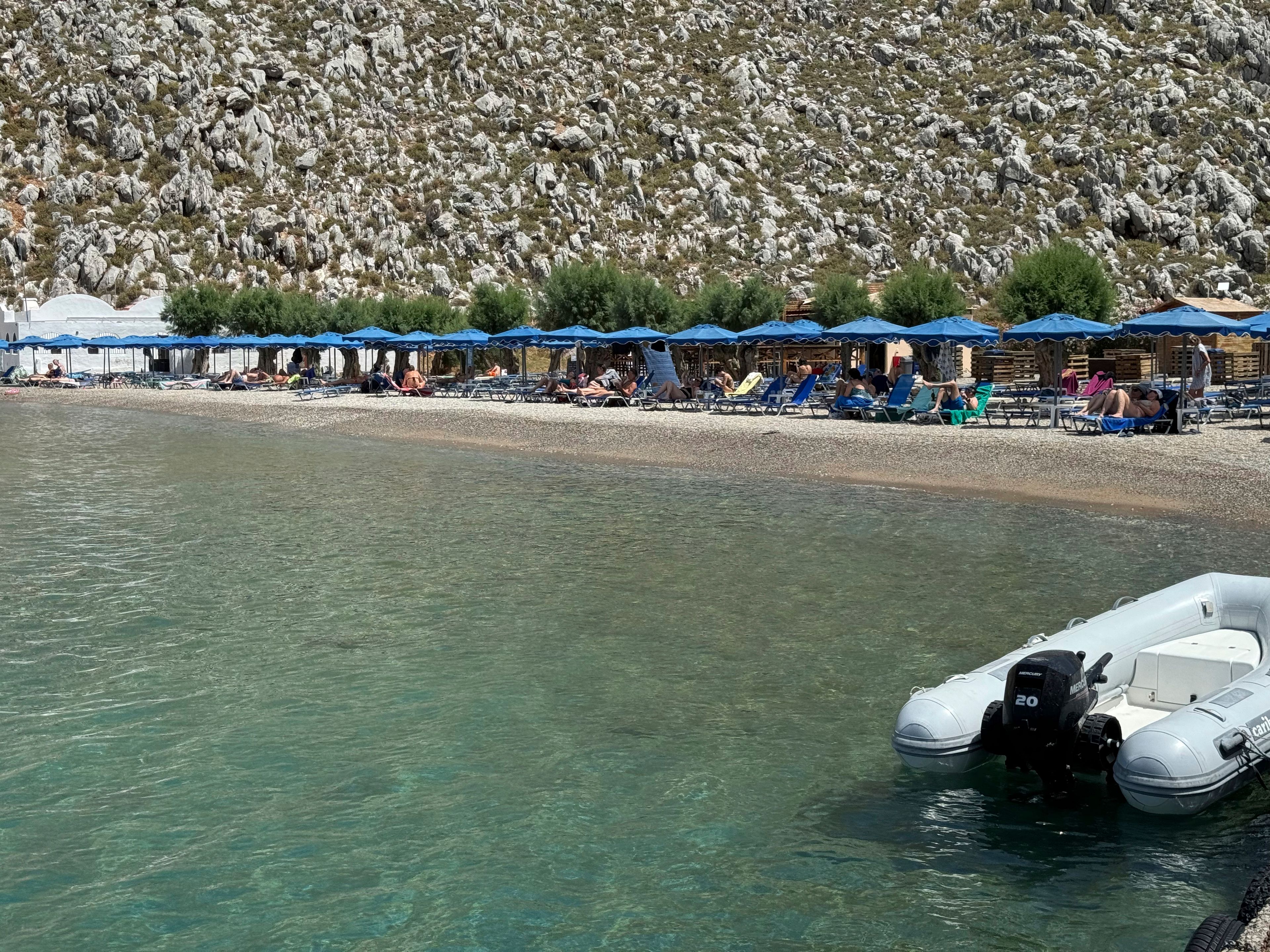 People sit on the beach of Agios Nikolaos from where British doctor and television presenter Michael Mosley, is believed to have set out, on the southeastern Aegean Sea island of Symi, Greece, Friday, June 7, 2024. Greek police say an ongoing major search and rescue operation on the small eastern Aegean island of Symi has still not located British doctor and television presenter Michael Mosley, who went missing on Wednesday afternoon after reportedly going for a walk.