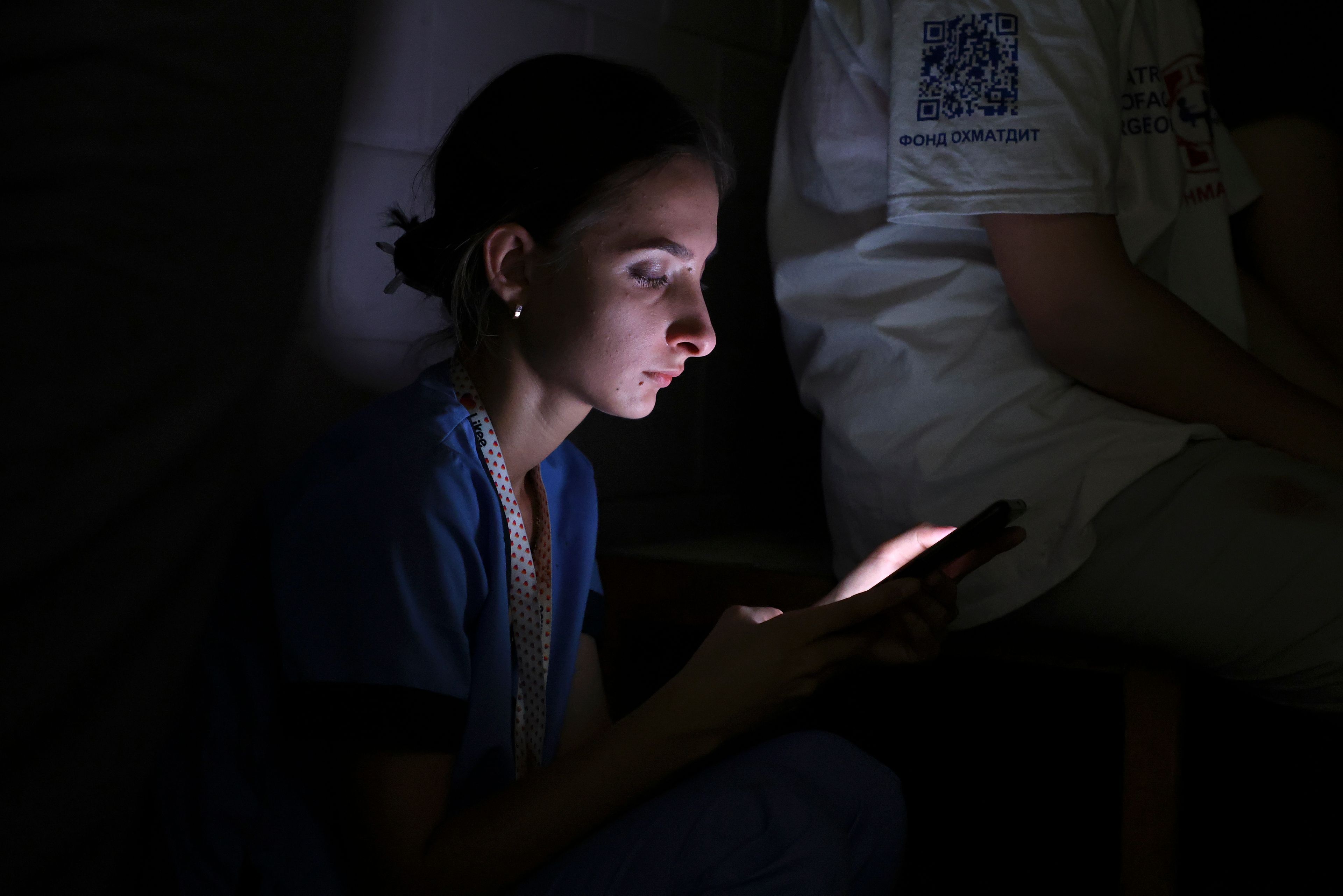 A nurse looks at her phone as she takes shelter in a basement after Russian missile hit the country's main children hospital Okhmadit in Kyiv, Ukraine, Monday, July 8, 2024. The daytime barrage targeted five Ukrainian cities with more than 40 missiles of different types hitting apartment buildings and public infrastructure, President Volodymyr Zelenskyy said on social media. (AP Photo/Anton Shtuka)