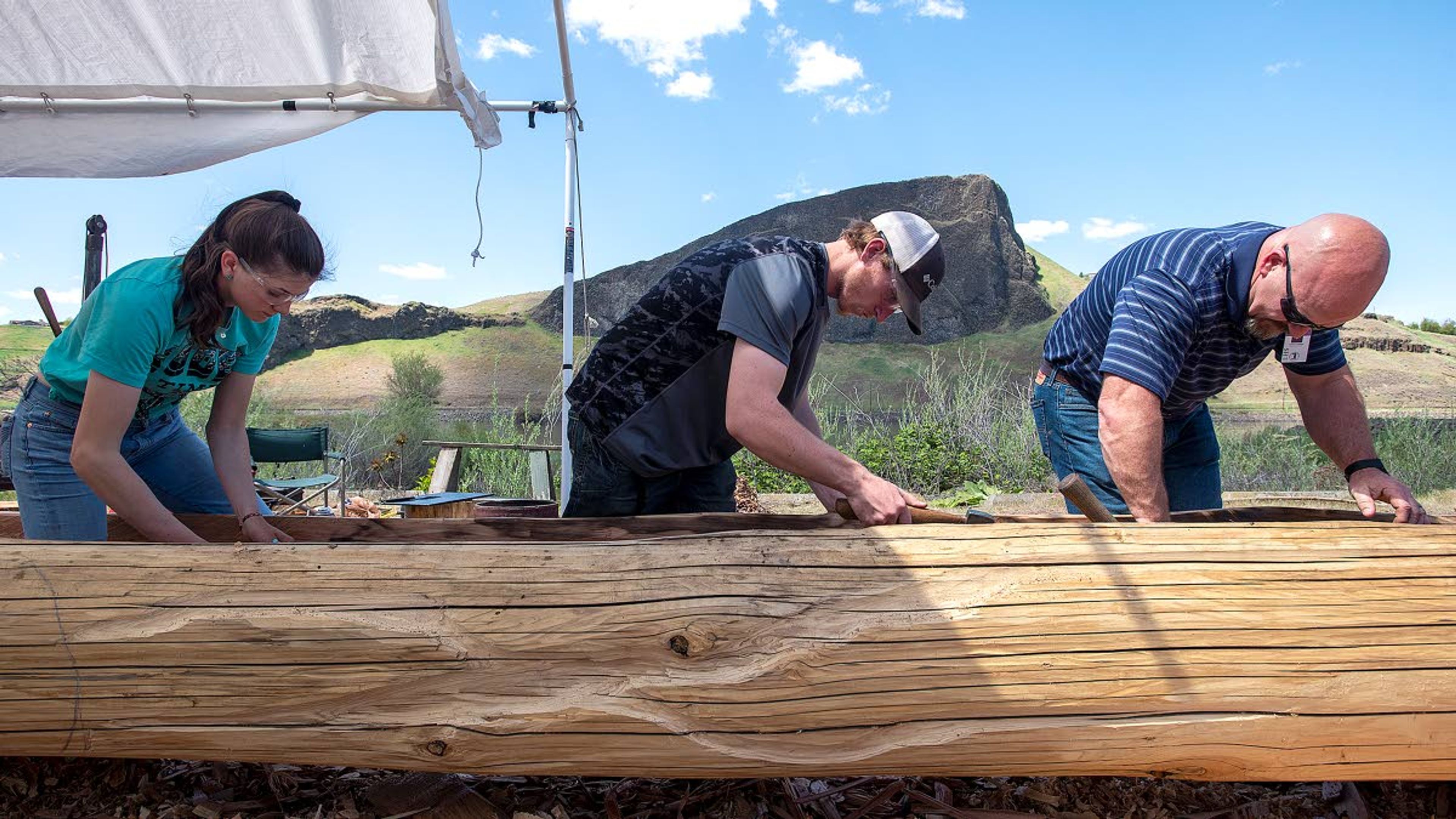 Meagan Wootton, left, Hunter Dunlap, center, and Stuart Johnson, who teaches the Construction 3 class at Lewiston High School, work on carving out the inside of a cedar log Monday afternoon at Hells Gate State Park. Johnson's class is helping with the construction of a dugout canoe that will go on display behind the park's Discovery Center.