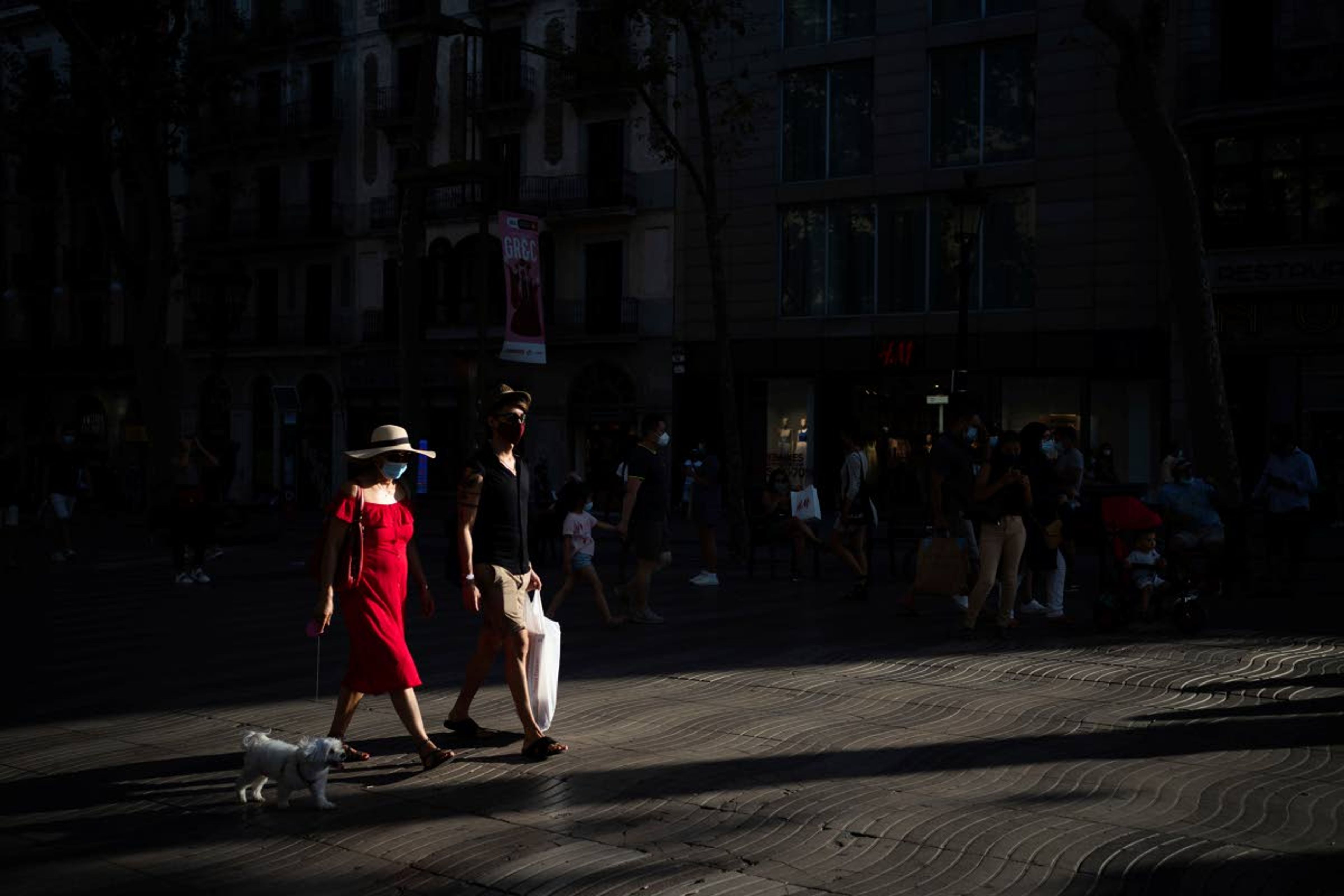 People wearing a face mask walk on Las Ramblas in Barcelona, Spain, Monday, July 27, 2020. Britain has put Spain back on its unsafe list and announced Saturday that travelers arriving in the U.K. from Spain must now quarantine for 14 days. (AP Photo/Felipe Dana)