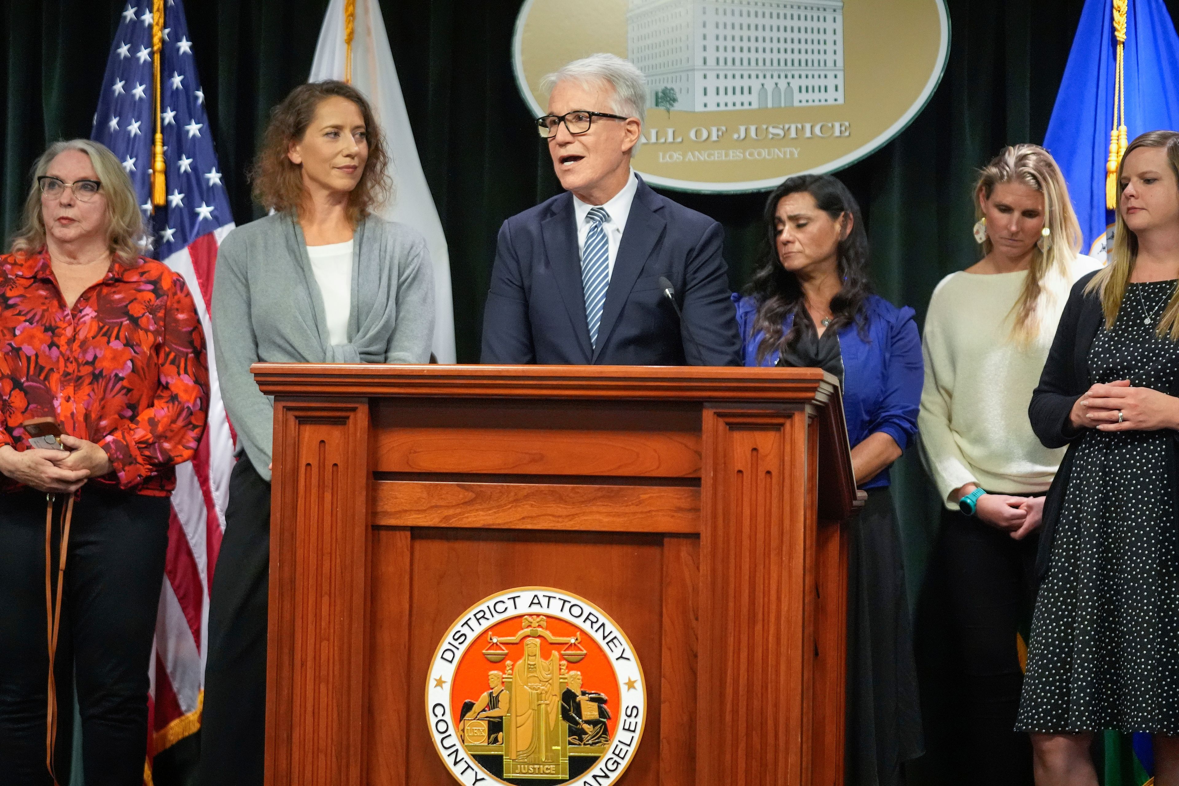 Los Angeles County District Attorney George Gascon, right, flanked by Menedez family members talks during a news conference at the Hall of Justice on Thursday, Oct. 24, 2024, in Los Angeles. (AP Photo/Damian Dovarganes)