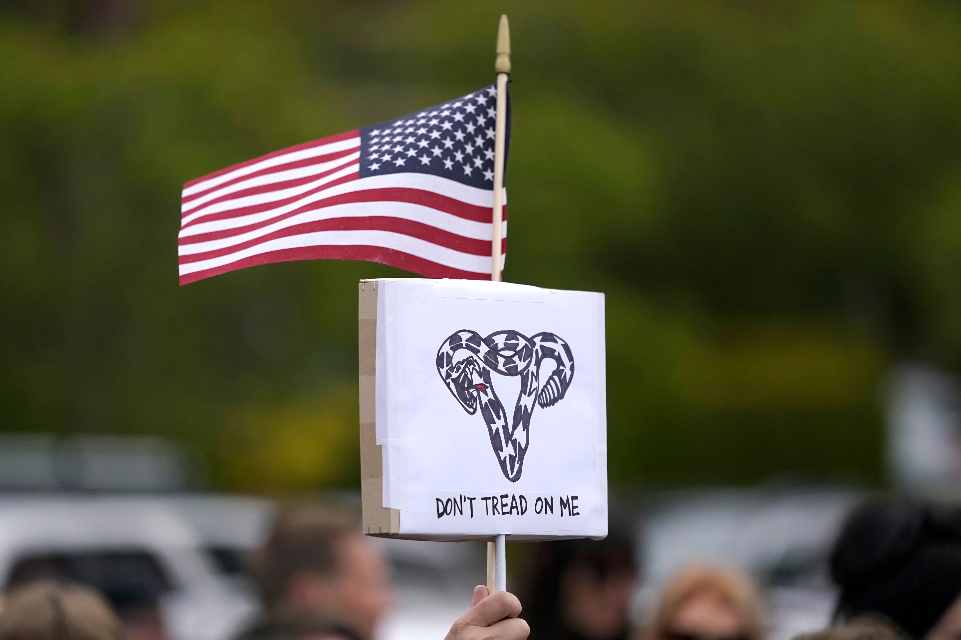 A person holds a sign that reads "Don't Tread On Me" with a uterus-shaped snake and a U.S. flag, Tuesday, May 3, 2022, during a rally at a park in Seattle in support of abortion rights. (AP Photo/Ted S. Warren)